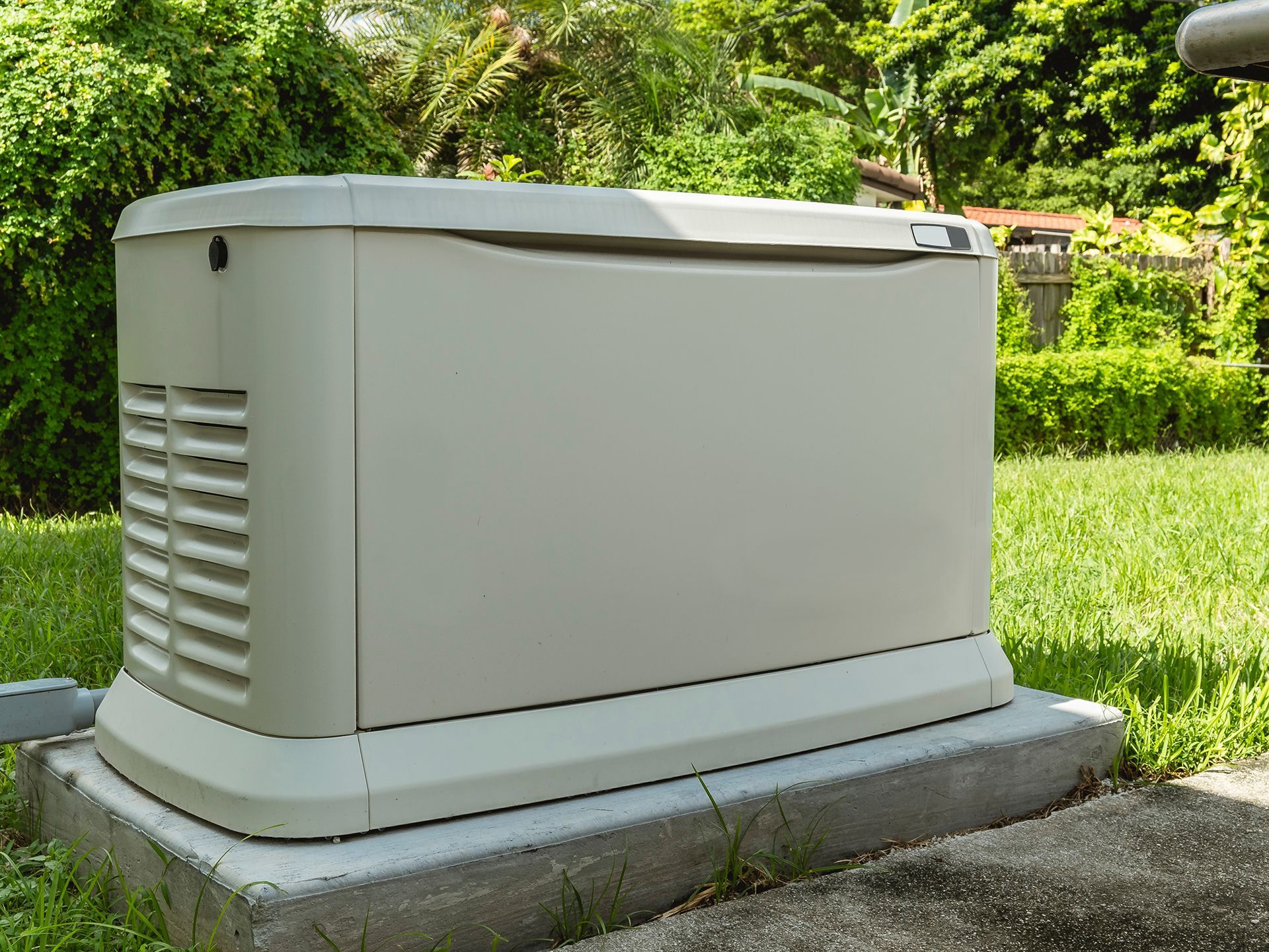 A white generator is sitting on top of a concrete block in the grass.