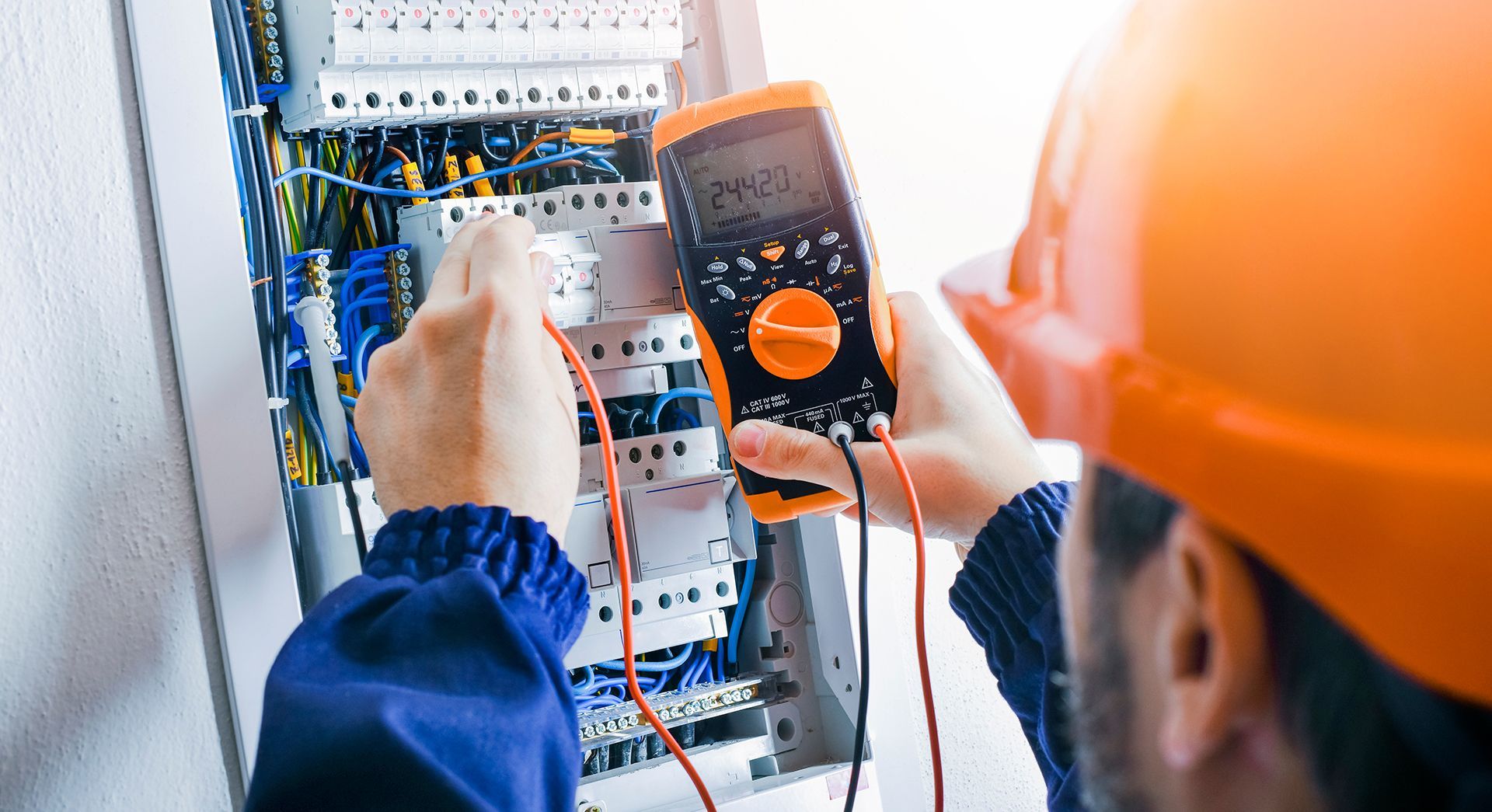 An electrician is using a multimeter to test an electrical box.