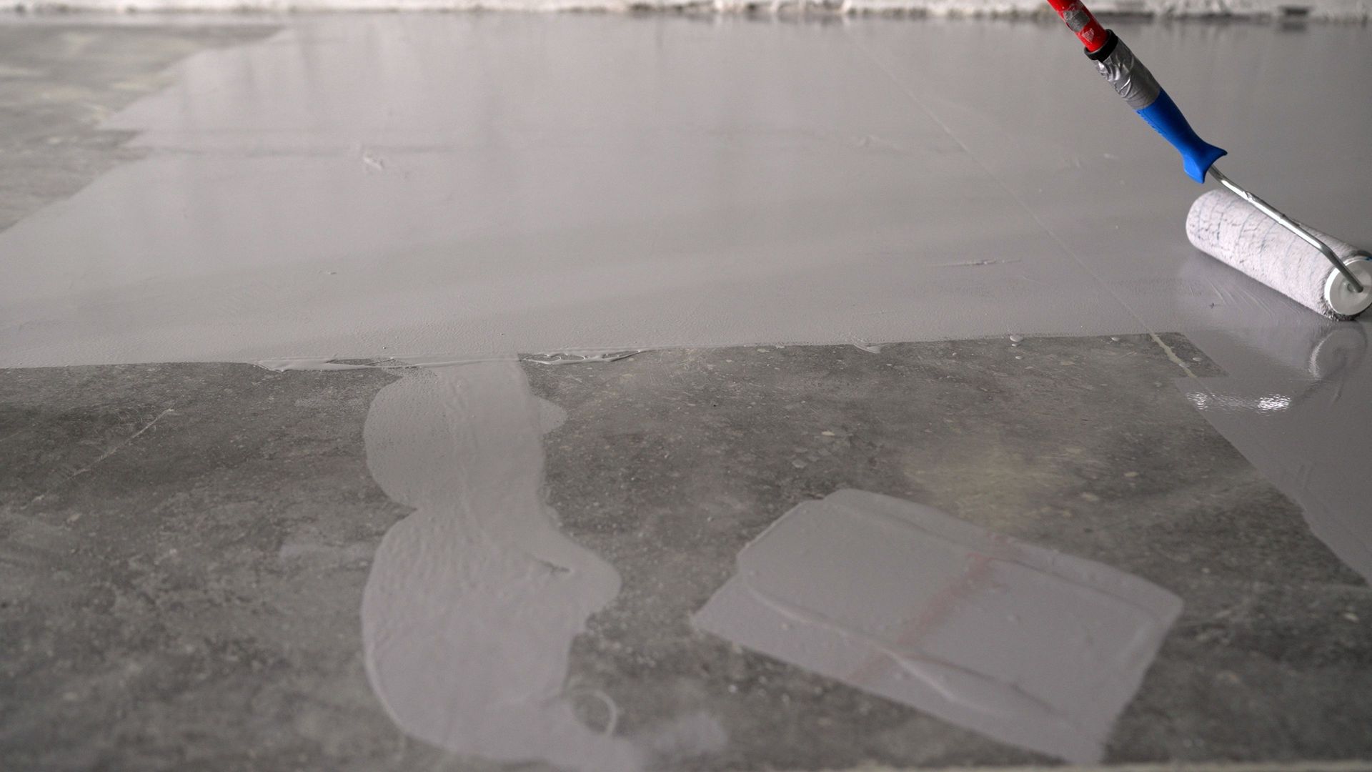 Painting a floor gray with a roller. White roller on blue handle applies paint.