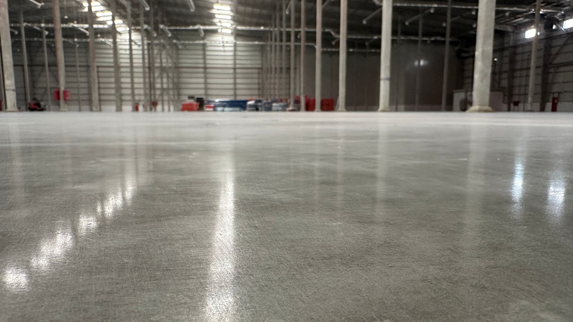 Large, polished concrete floor inside a warehouse, reflecting overhead lights.