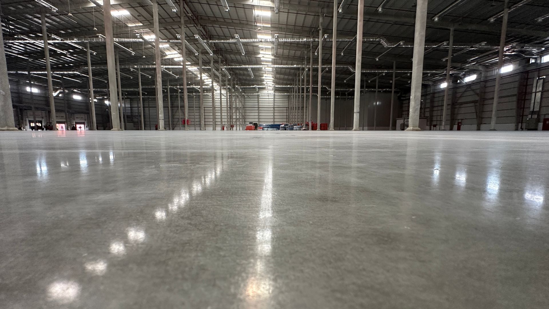 Polished concrete floor inside a large warehouse, reflecting overhead lights.