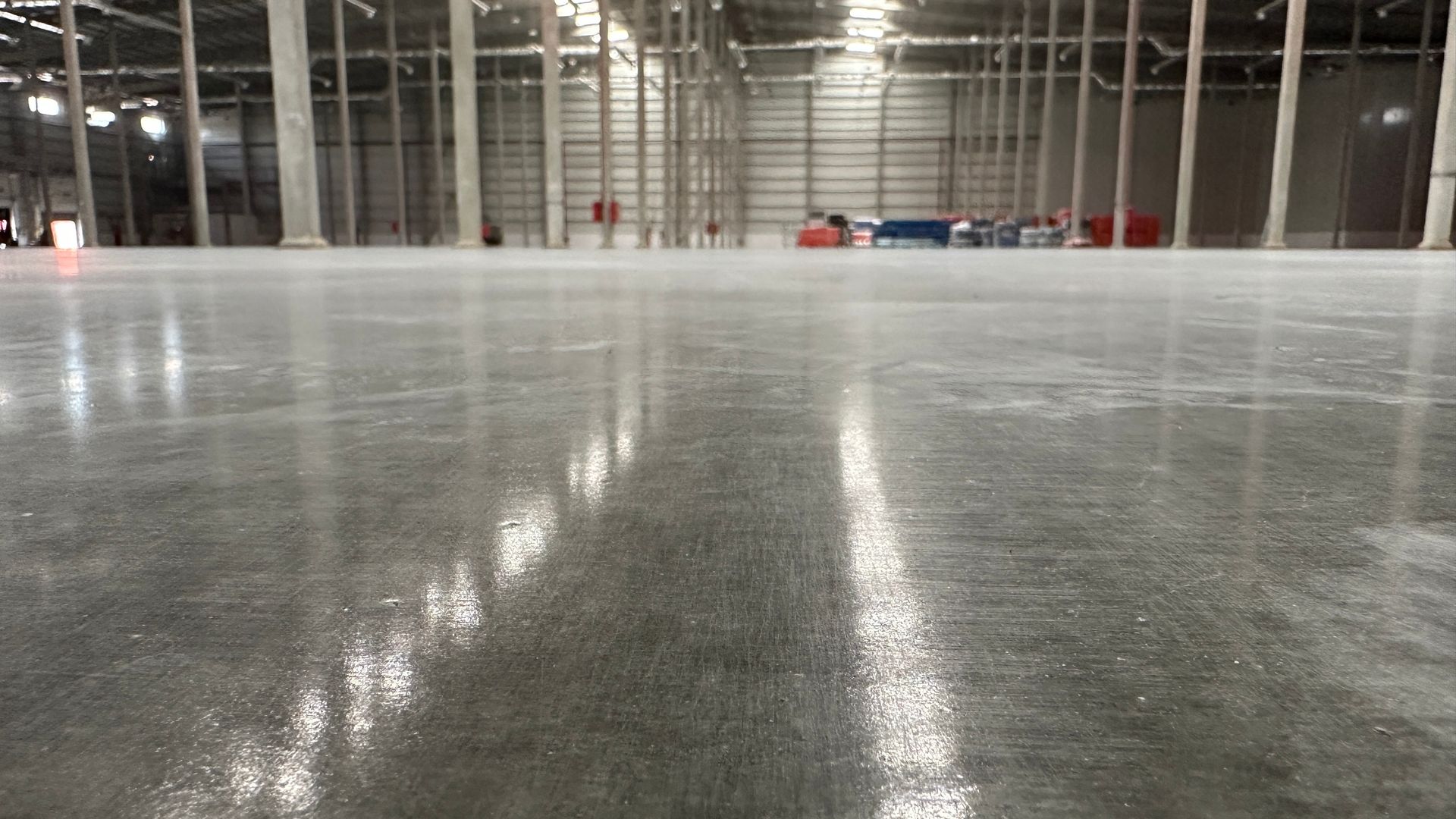 Polished concrete warehouse floor with reflections, columns in the background.