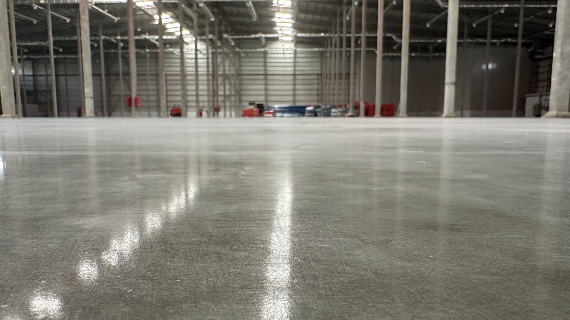 Polished concrete floor inside a large warehouse, reflecting overhead lights.