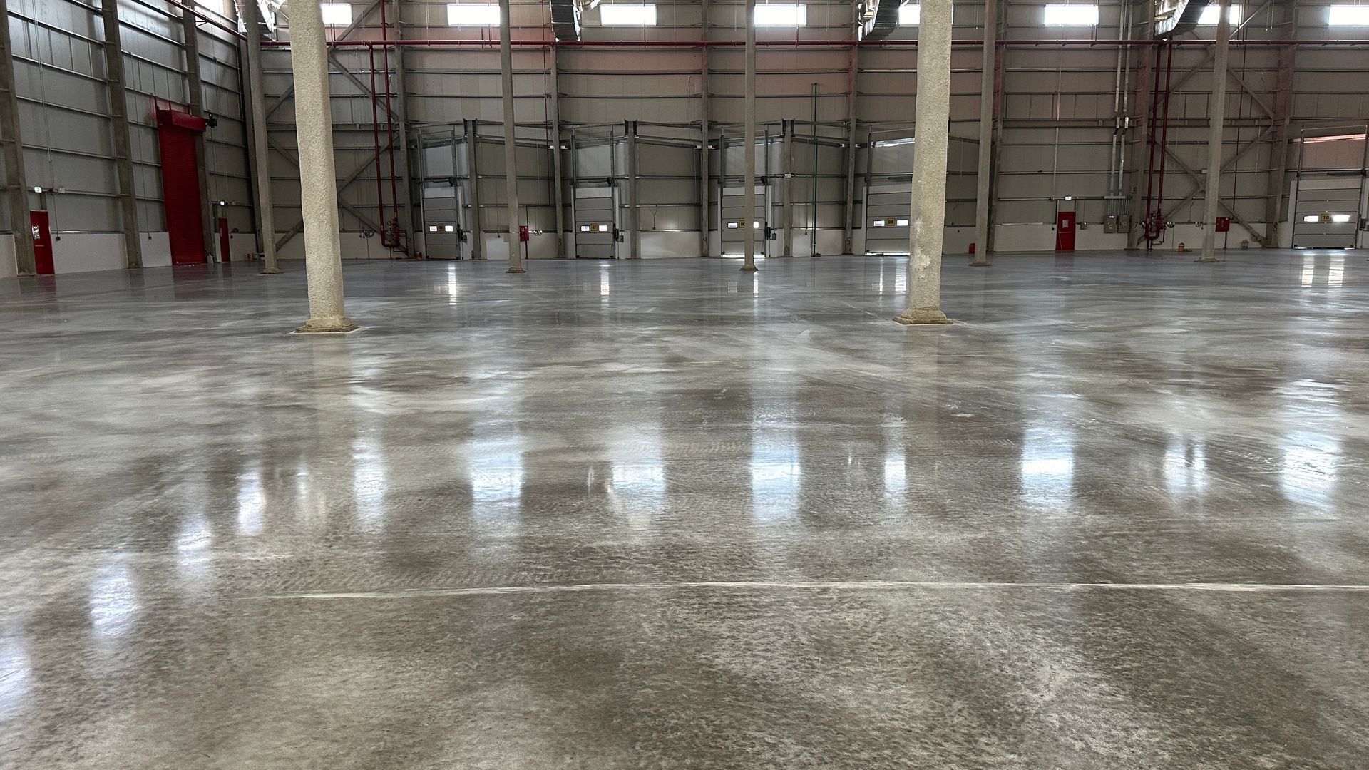 Inside a large, empty warehouse with polished concrete floors, tall columns, and overhead lighting.