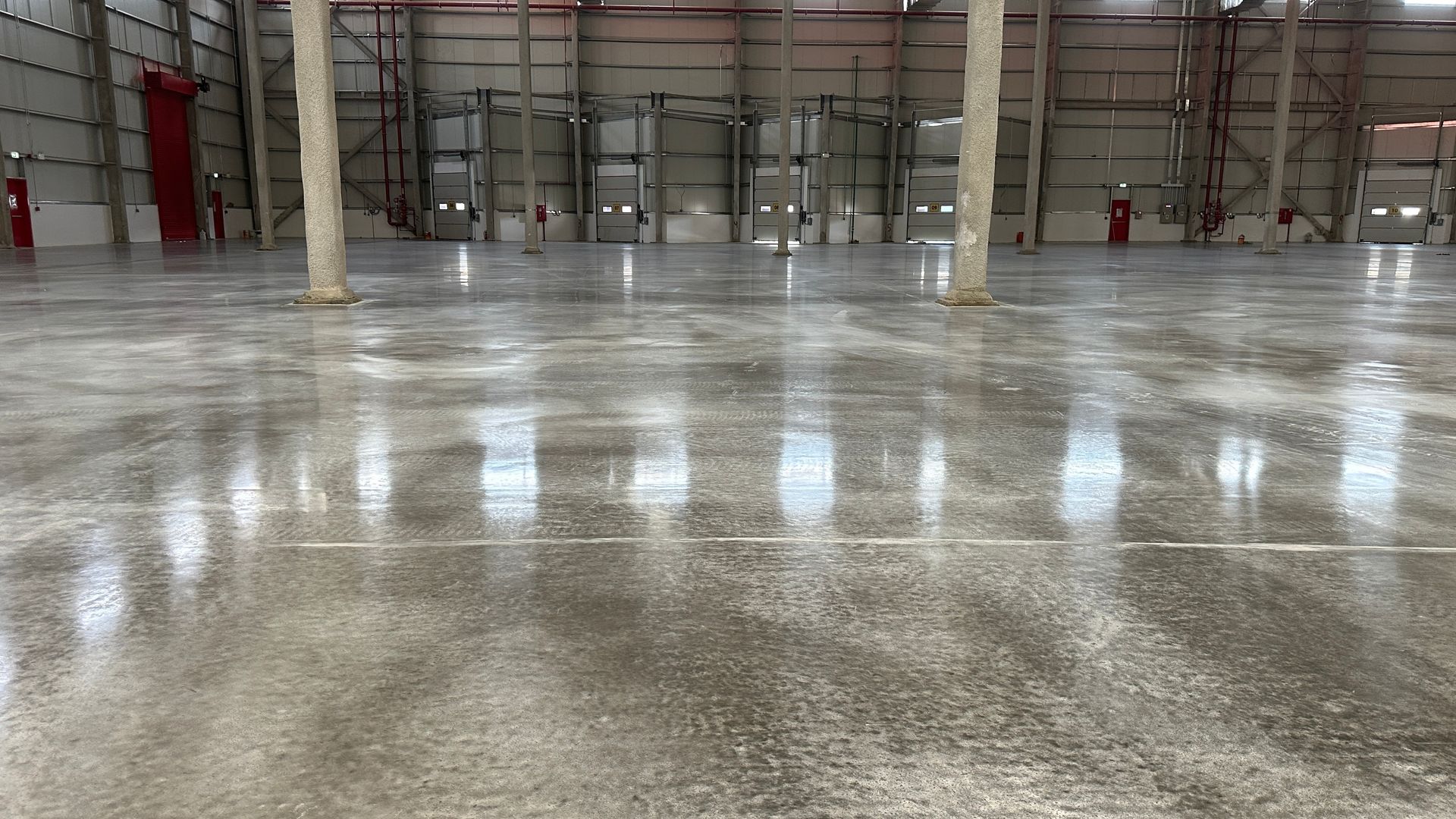 Wide shot of a polished concrete floor in a large warehouse. Columns are visible, along with doors and metal framework.