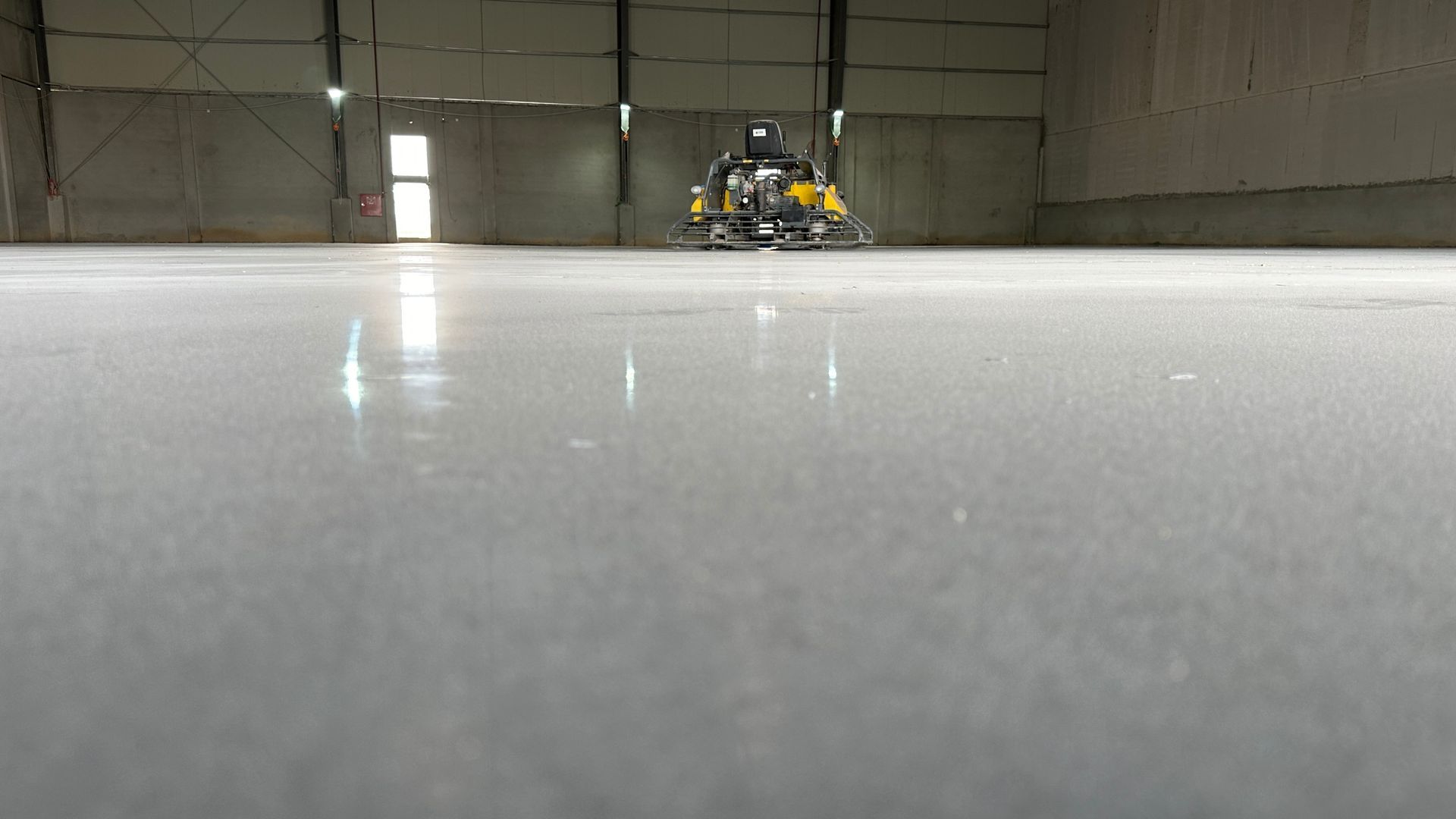 Polished concrete floor being cleaned by a machine inside a large warehouse.