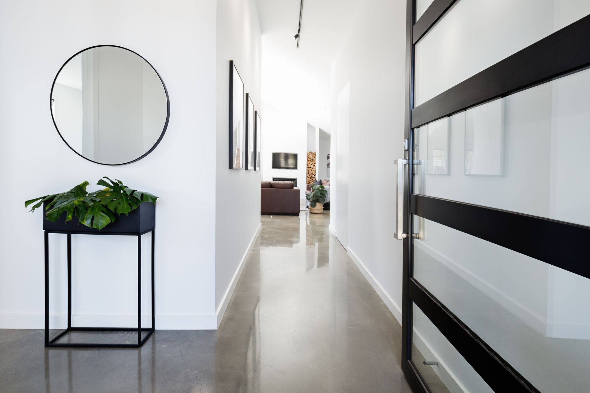 Modern hallway with black and white accents. Black planter, round mirror, and glass door.