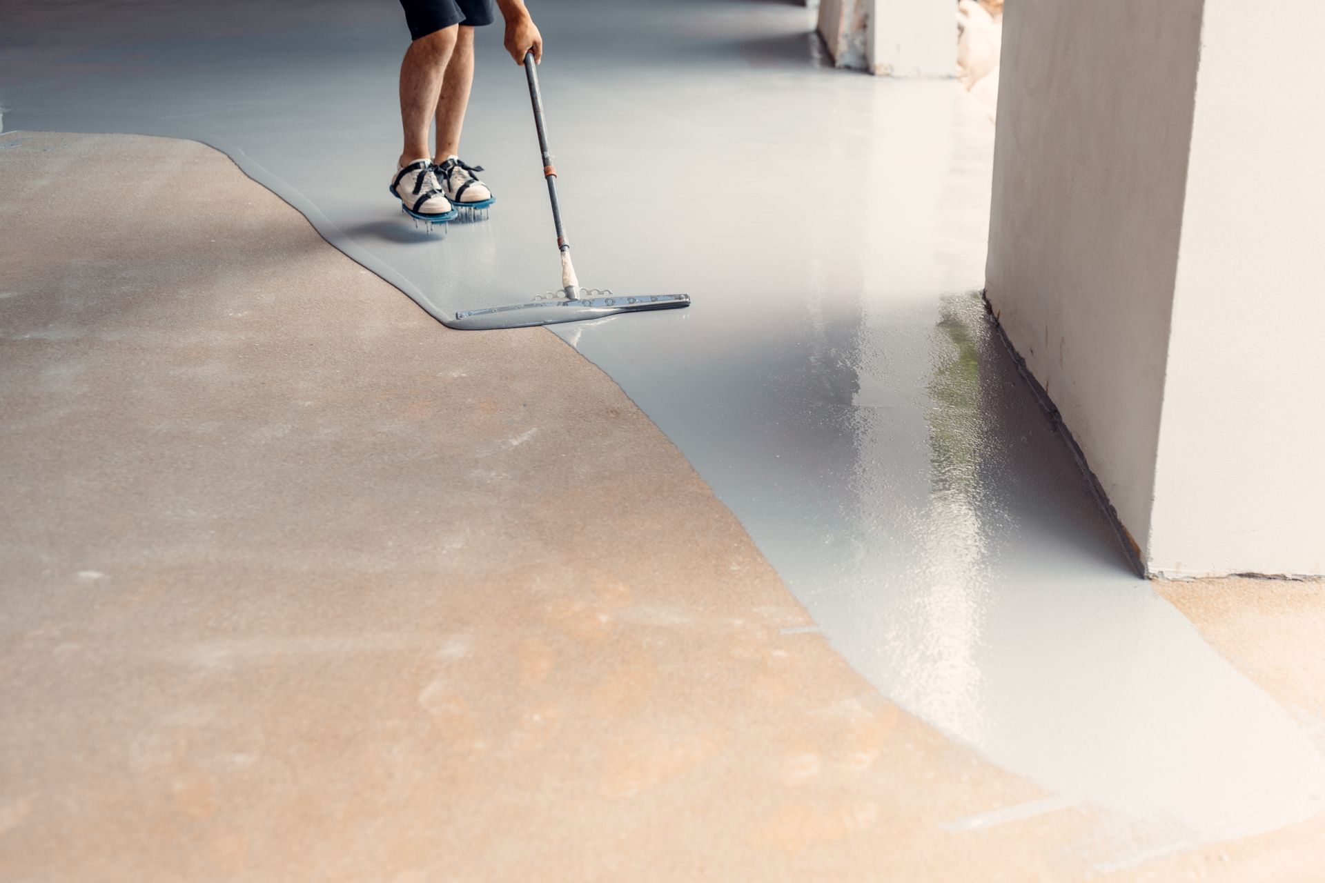 Person applying gray epoxy coating to a concrete floor with a mop.