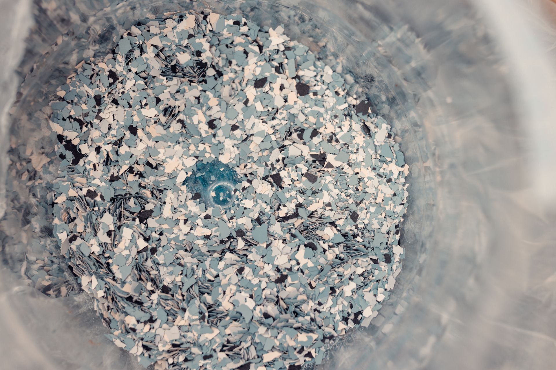 Blue, black, and white decorative floor flakes inside a translucent bucket.