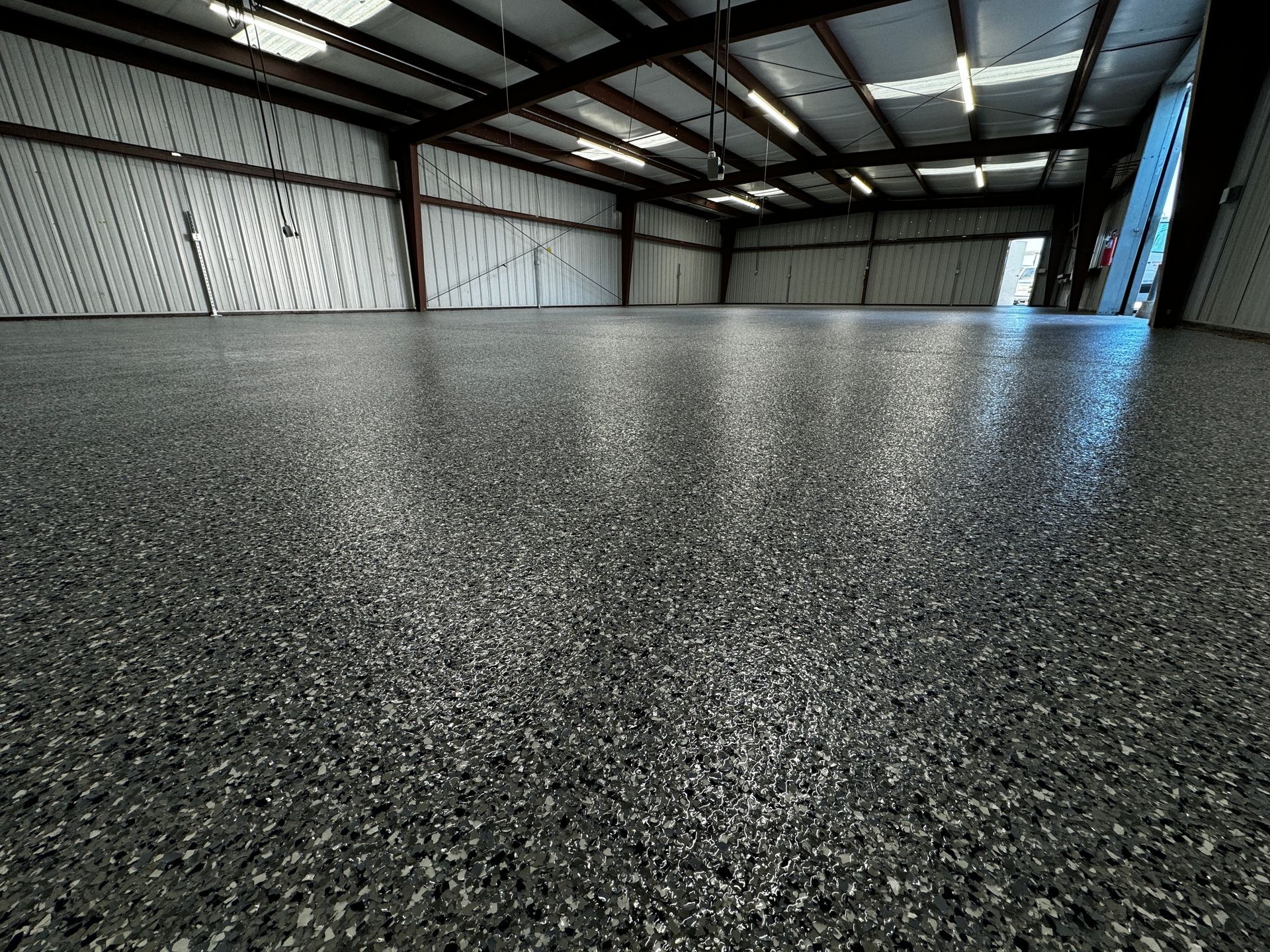 Spacious warehouse interior with a glossy, speckled floor reflecting overhead lights.