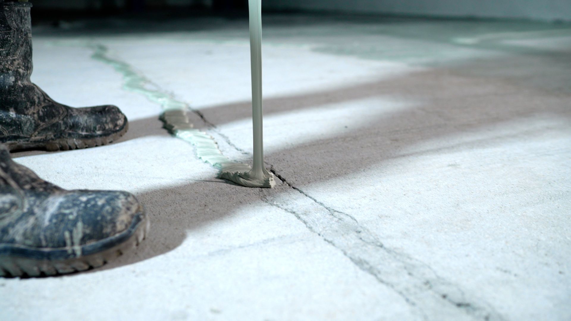 Person in rubber boots pouring sealant into a crack in a concrete floor.