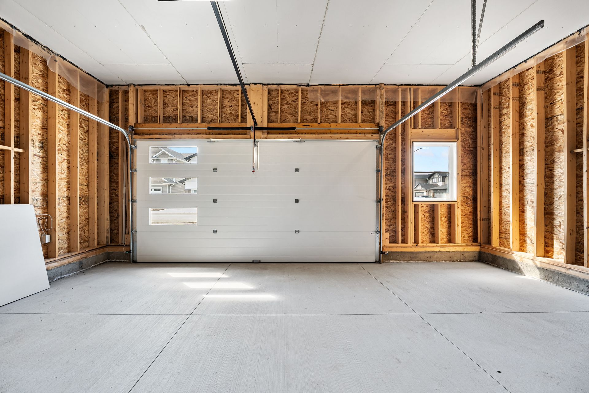 Unfinished garage interior with open white garage door, light wood framing, and concrete floor.