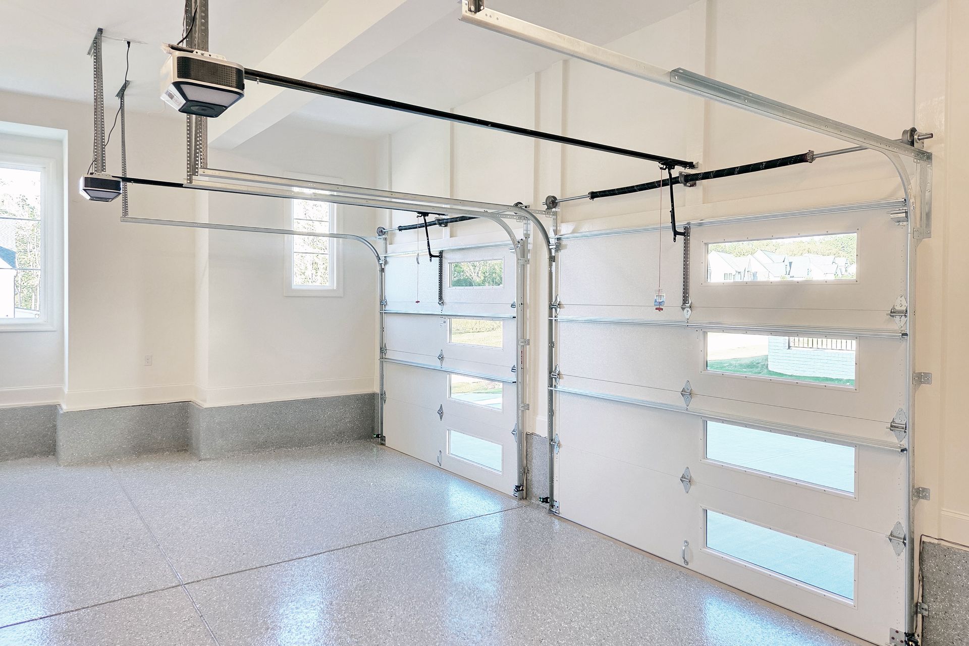Interior view of a clean, bright garage with epoxy floor and two overhead doors partially open.