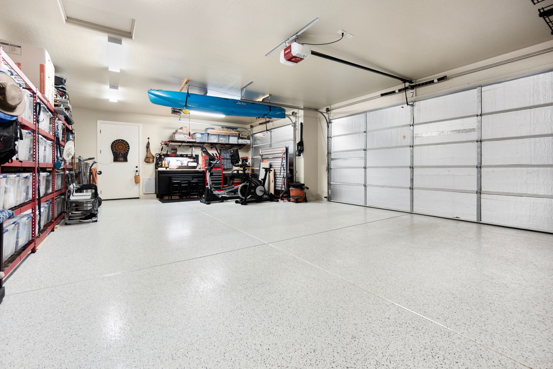 Brightly lit, clean garage with white speckled floor, tools, storage shelves, and overhead kayak.