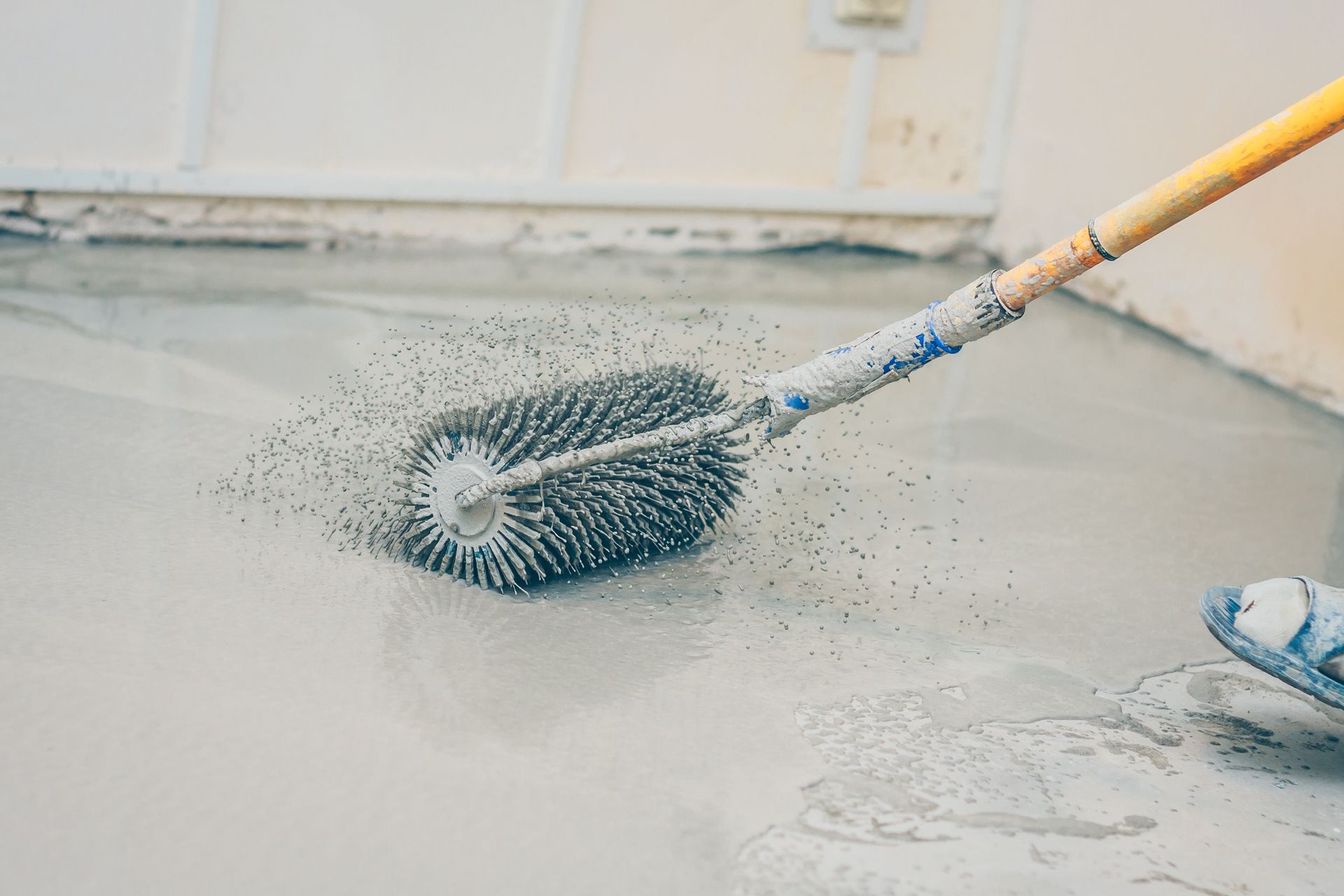 Person using a spiked roller to level wet concrete flooring.
