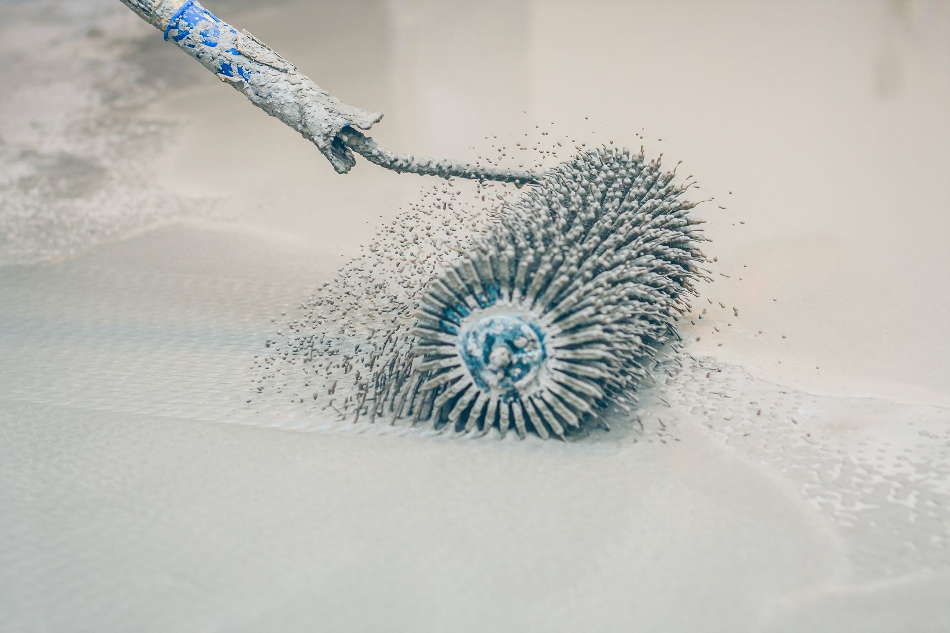 Roller tool with many spikes rolling over light gray surface.