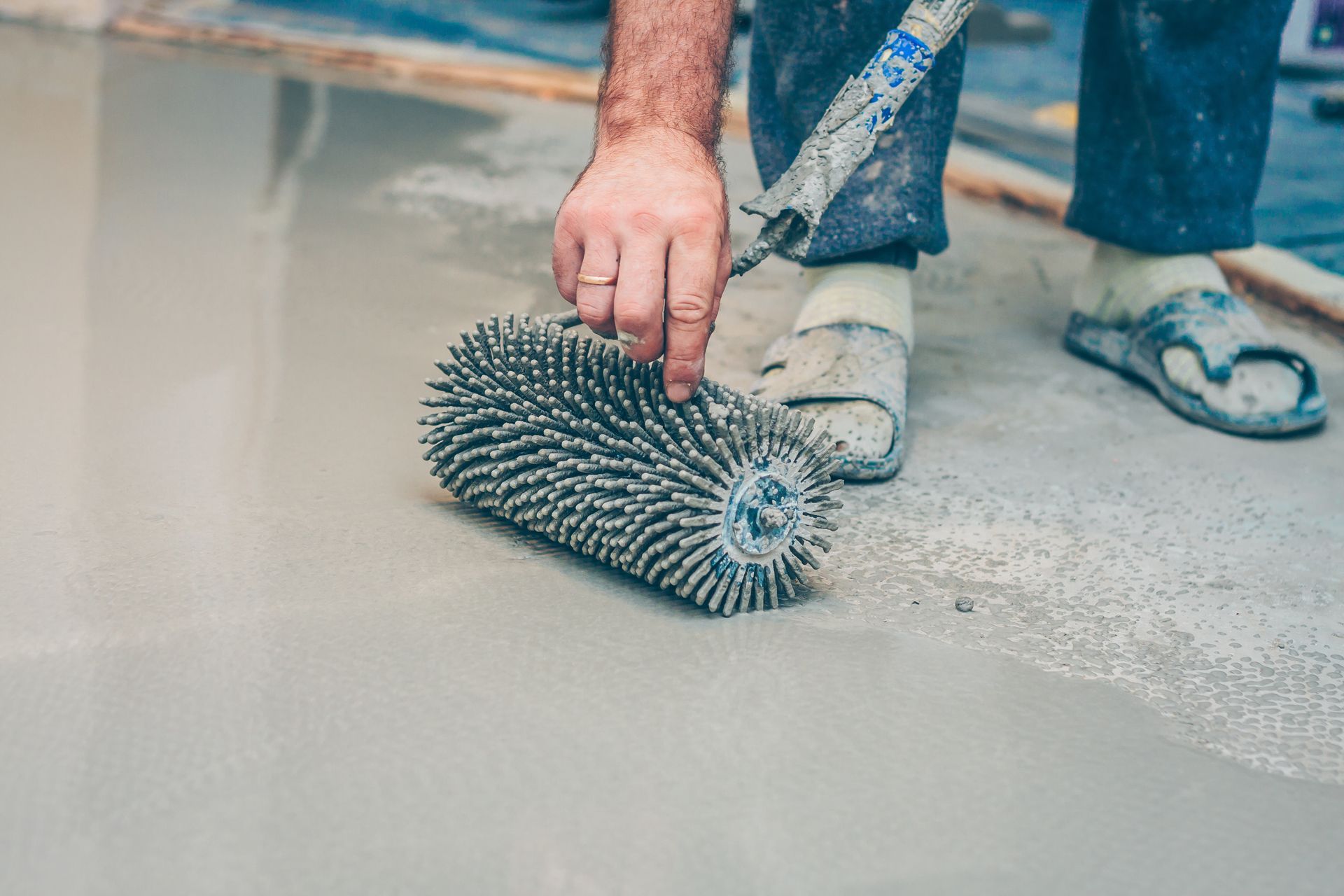 Person using a spiked roller on a gray concrete floor.