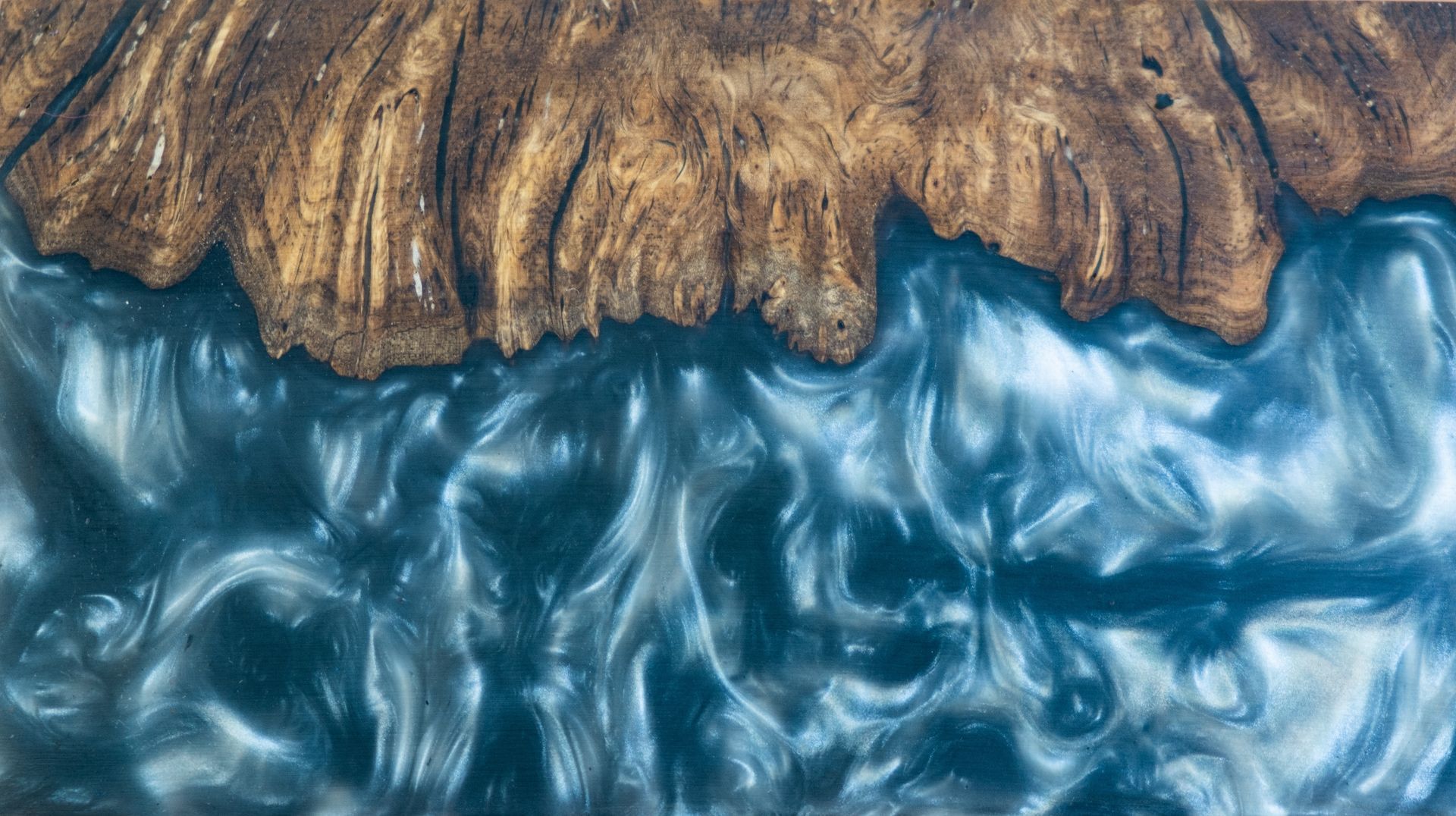 Wood table surface with brown burl wood and blue resin resembling a flowing ocean.