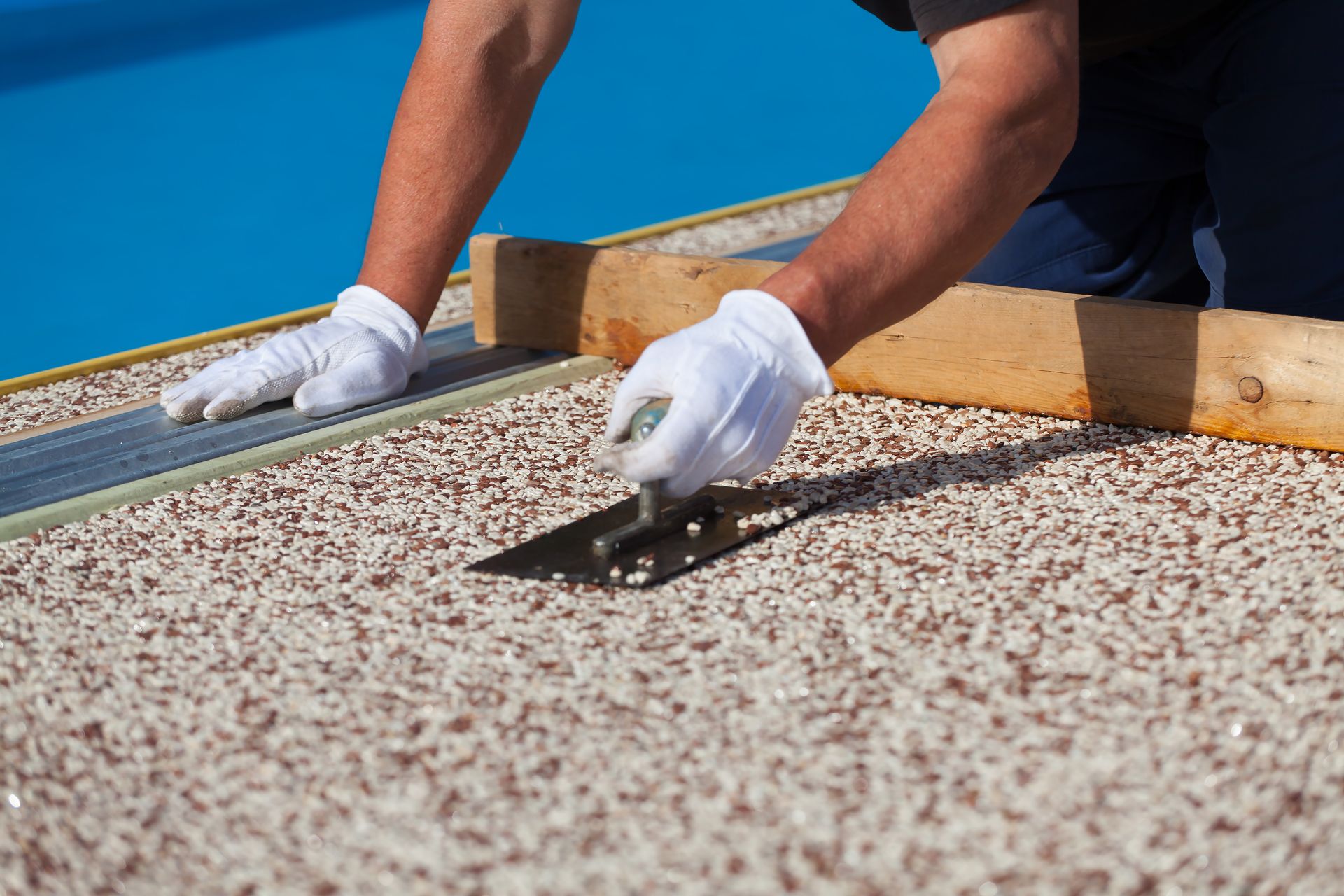 Person using a trowel to apply aggregate material near a pool.
