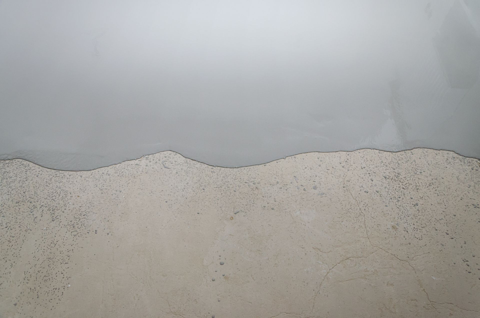 Gray liquid poured over a textured, light beige surface, creating a jagged edge.