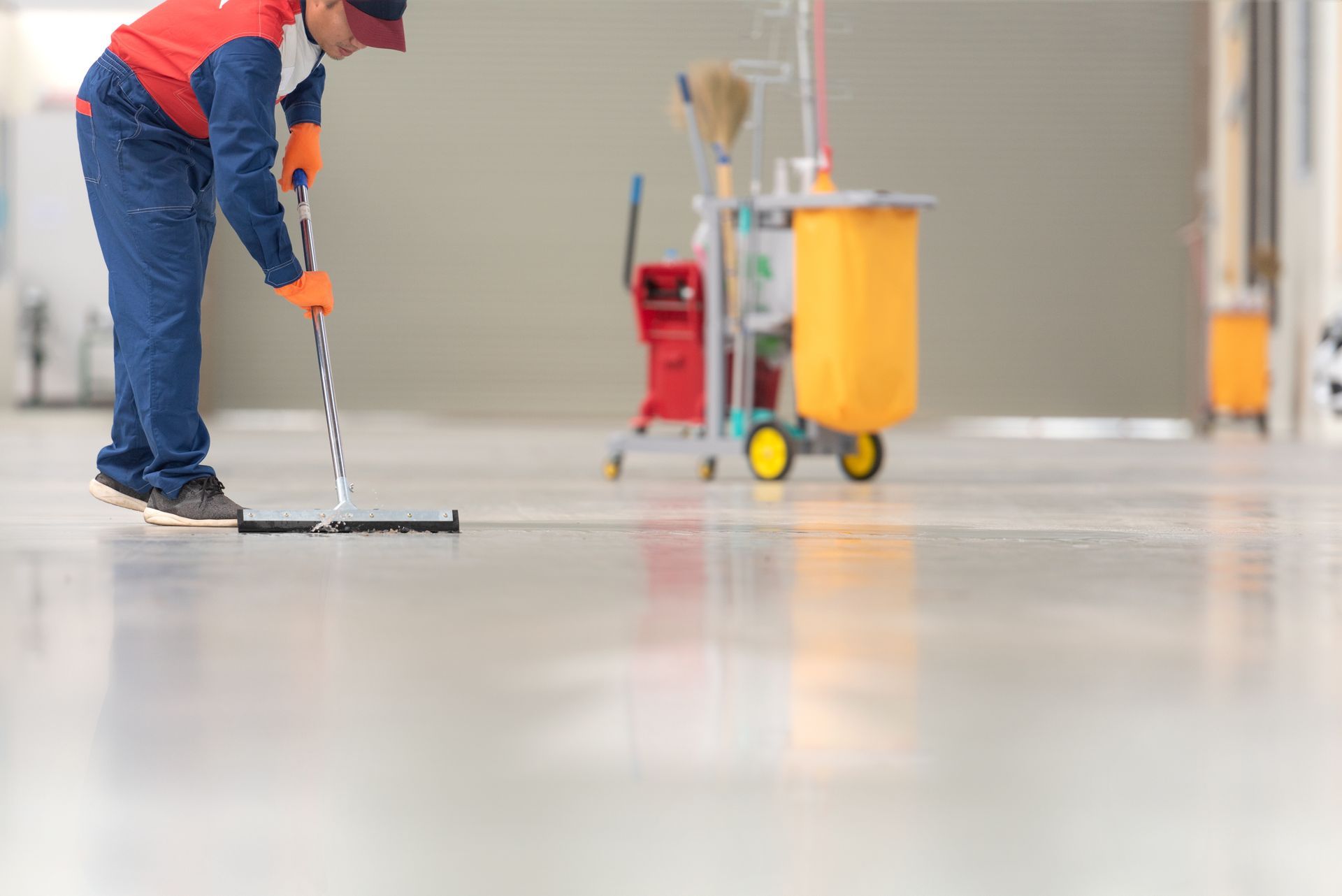 Person mopping a shiny, light-colored floor; cleaning cart with yellow bucket in background.