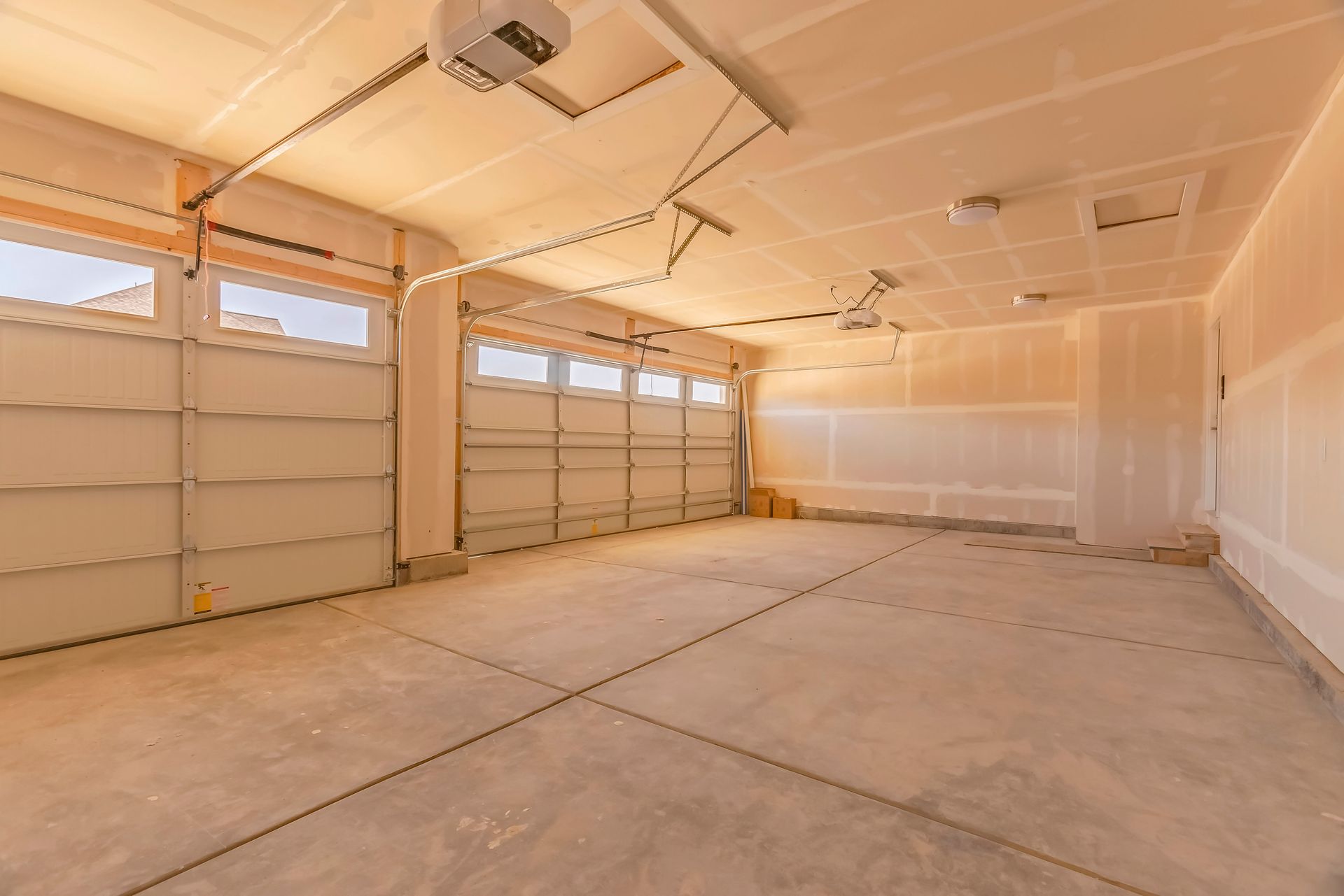 Empty unfinished garage with two garage doors and concrete floor.