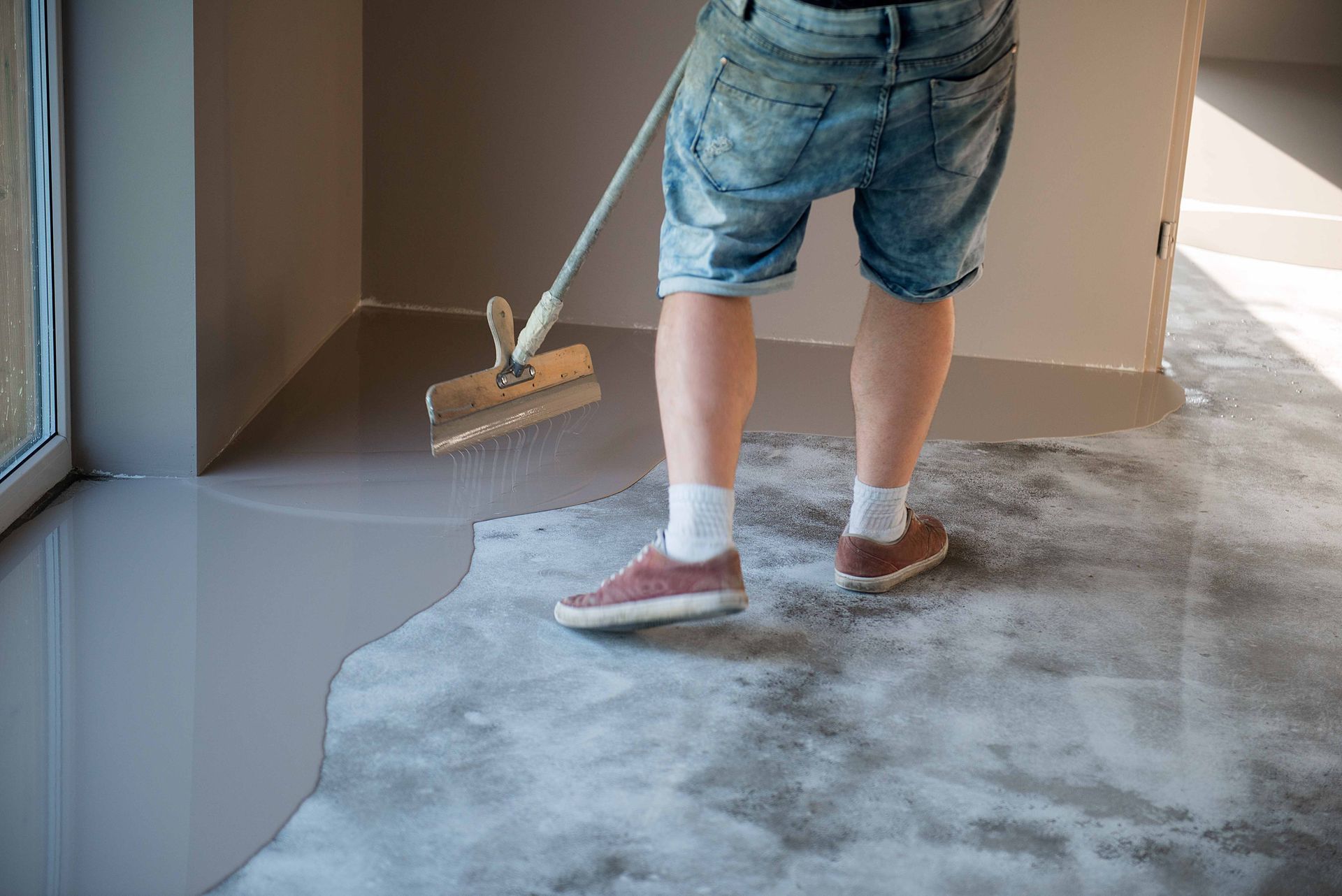Person using a tool to smooth out gray flooring in a room.