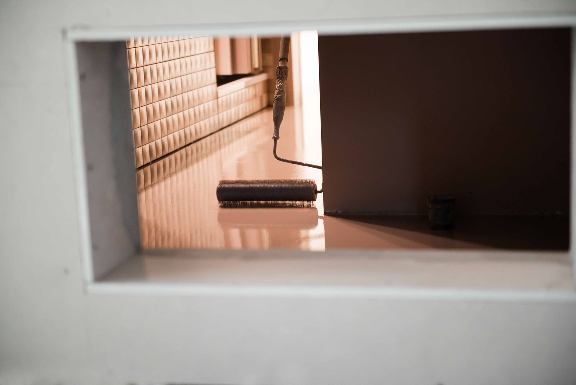 Paint roller on a shiny floor, viewed through a rectangular opening.