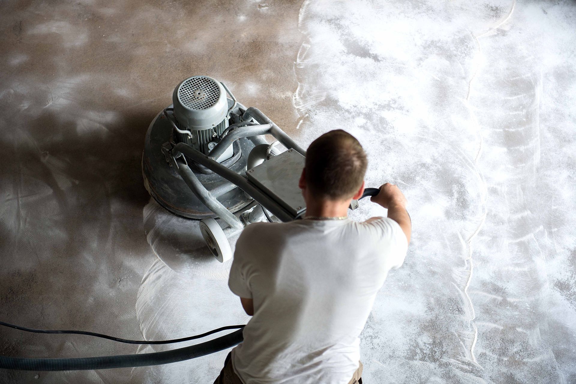 Person grinding a floor with a large machine, creating a white, dusty area on a brown floor.