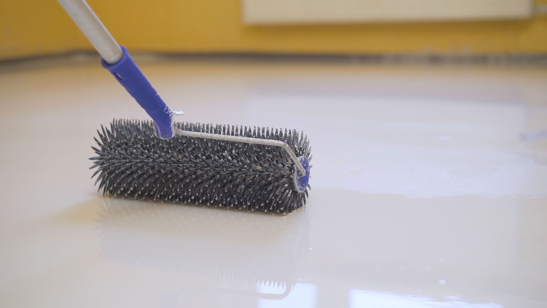 A floor being leveled with a spiked roller, used for epoxy application.