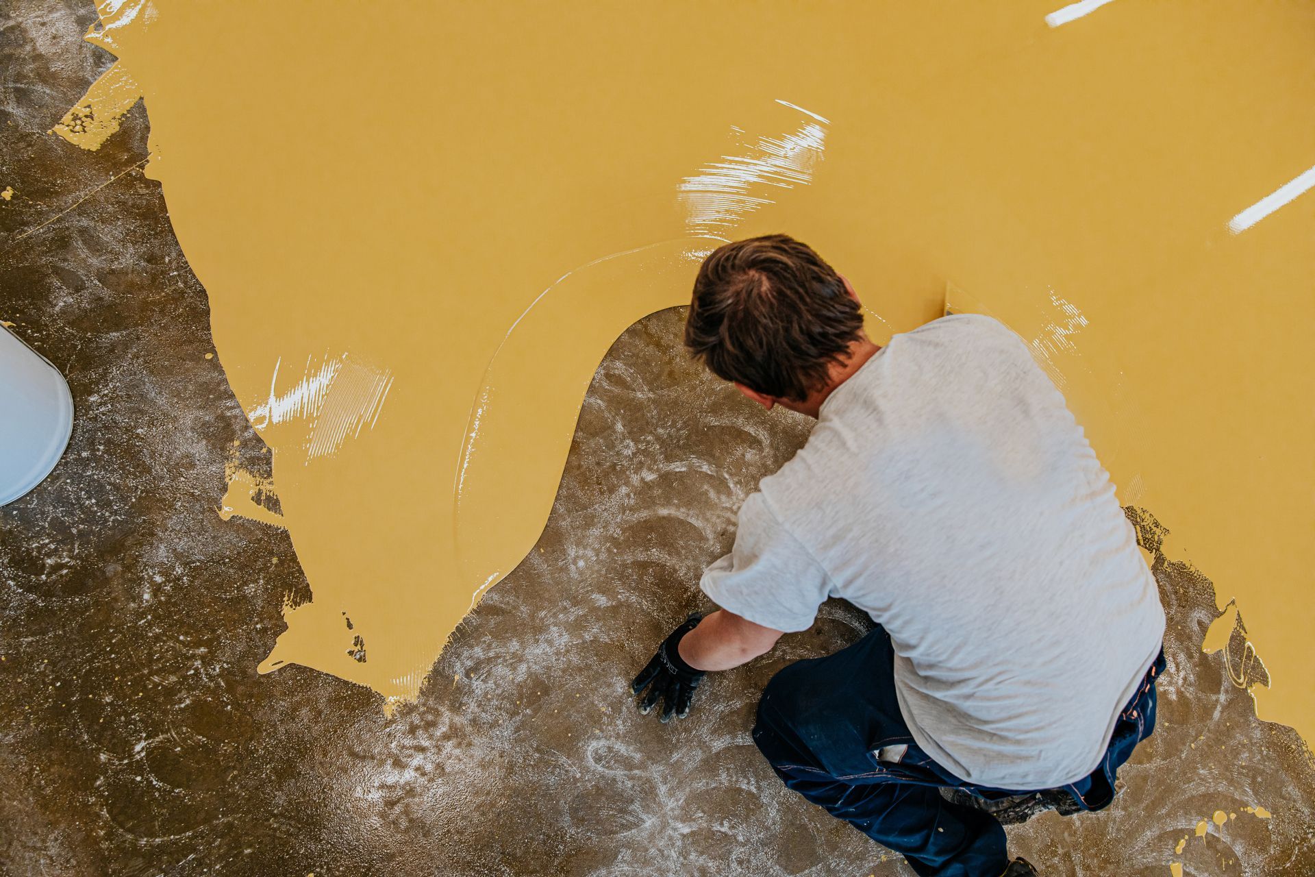 Person kneeling, applying yellow paint to a floor with a brush.