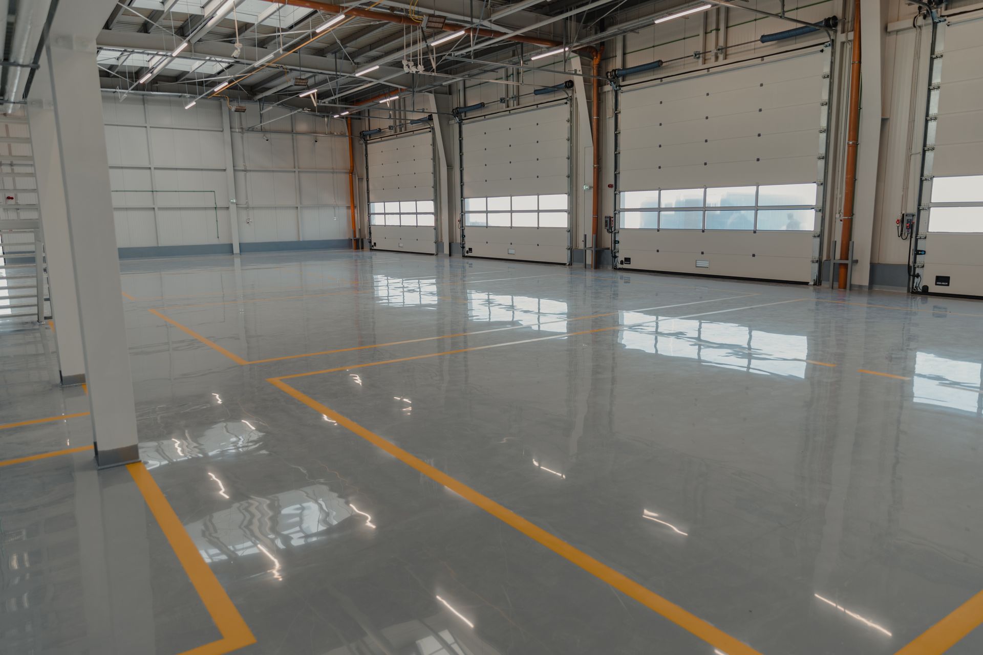 Empty, large industrial warehouse with gray floor, yellow lines, and closed garage doors.