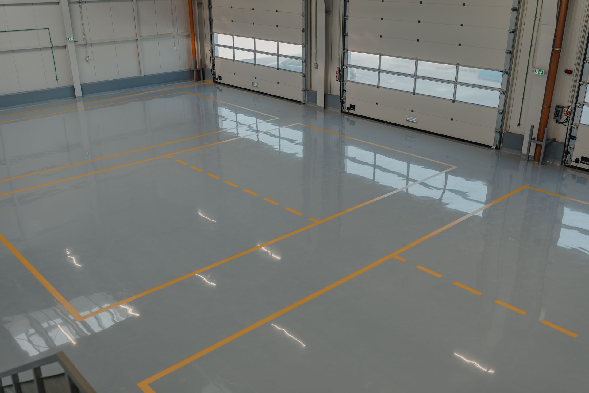 Large, empty warehouse interior with glossy gray floor, yellow lines, and closed garage doors.
