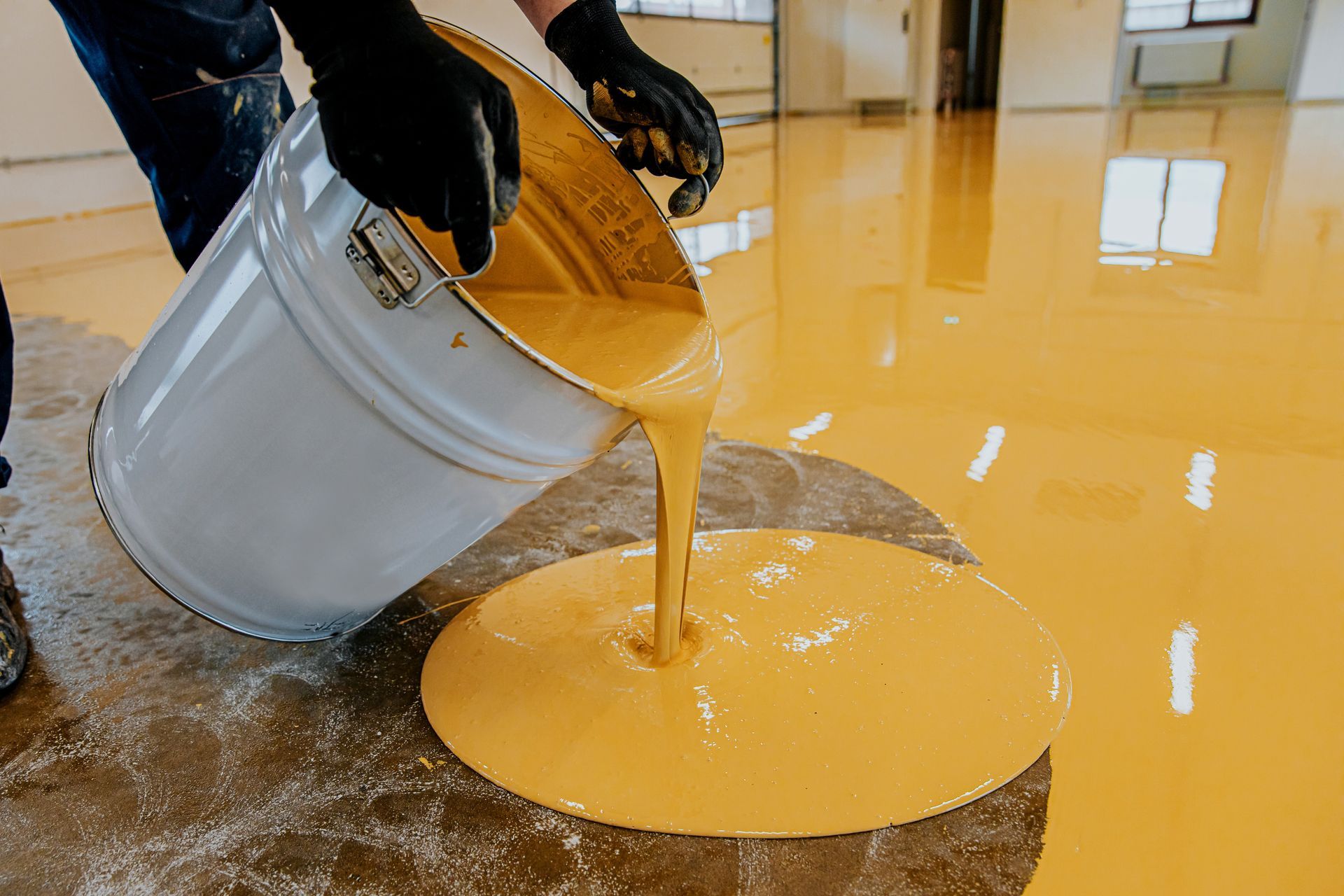 Person pouring yellow epoxy from a bucket onto a floor.