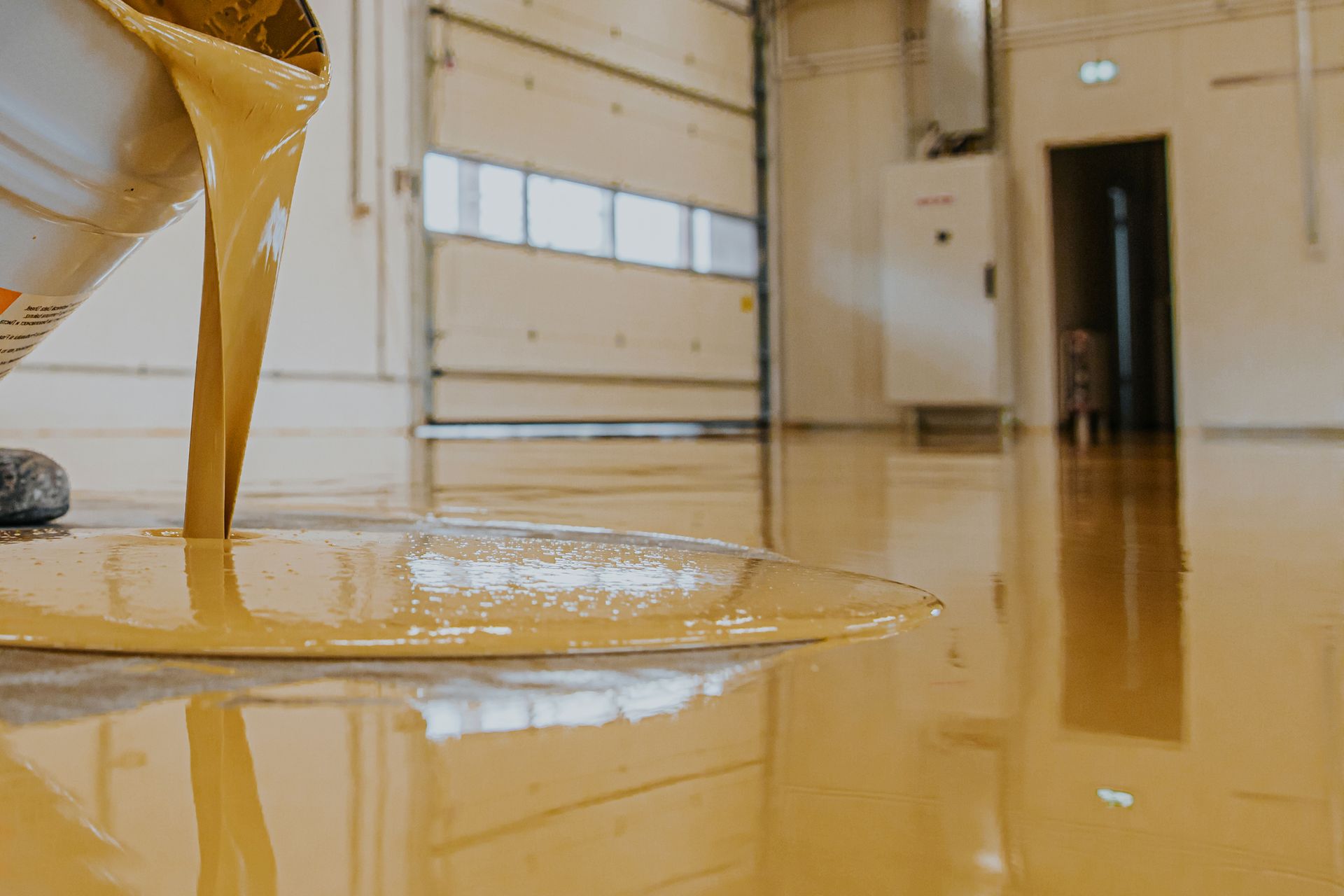Yellow liquid epoxy being poured onto a concrete floor inside a garage.
