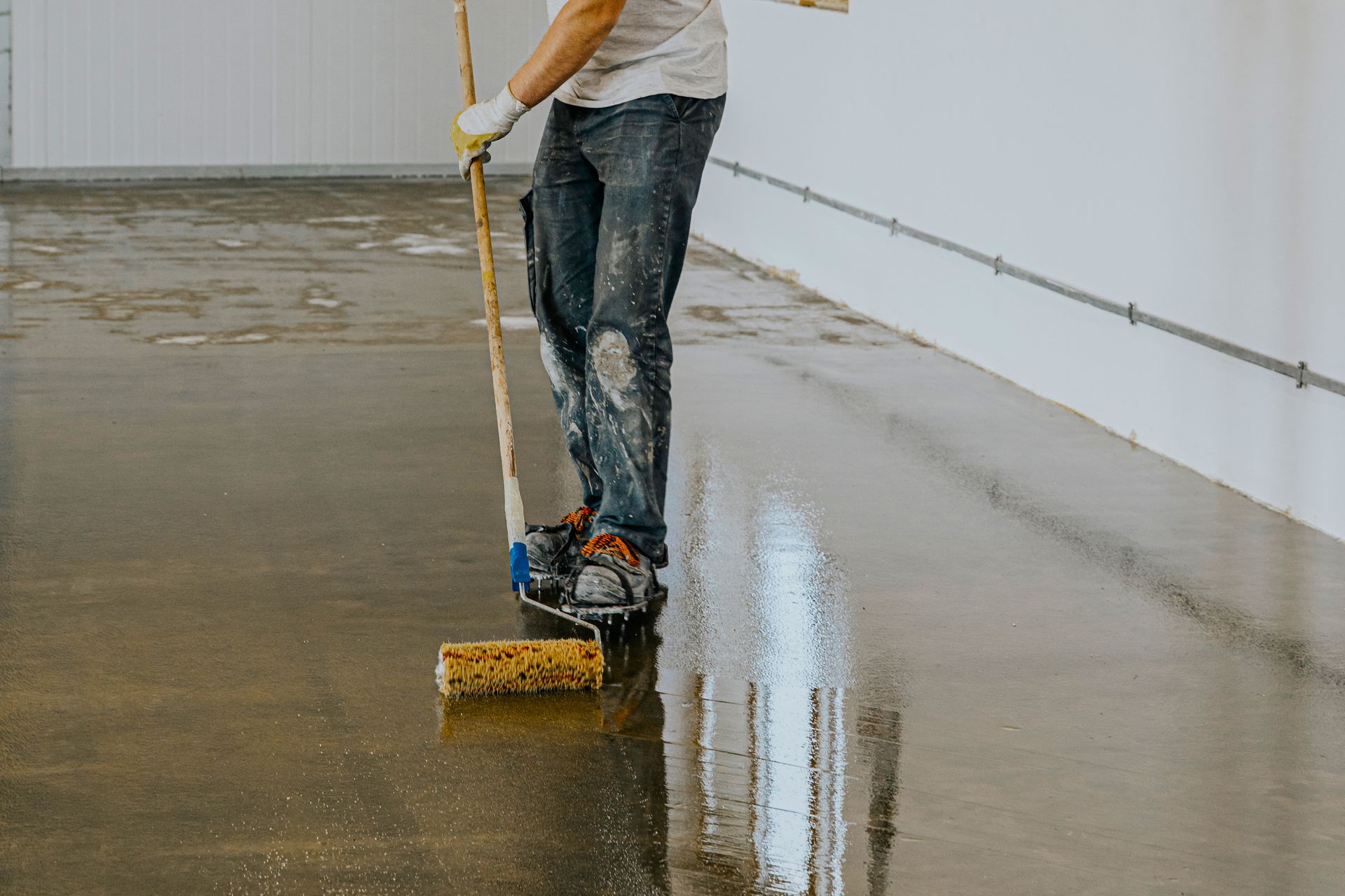 Person applying a sealant to a concrete floor with a roller. The floor is shiny and wet.