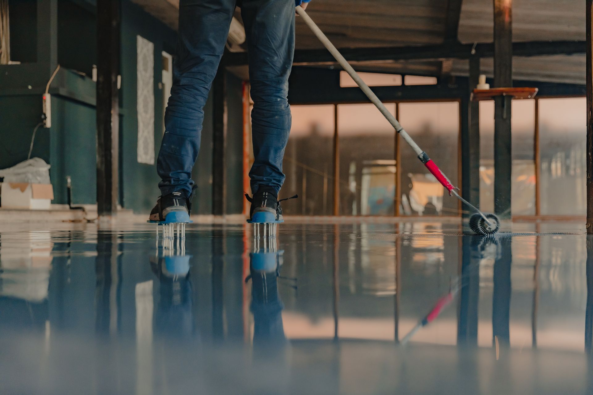 Person rolling blue epoxy coating on a reflective floor.