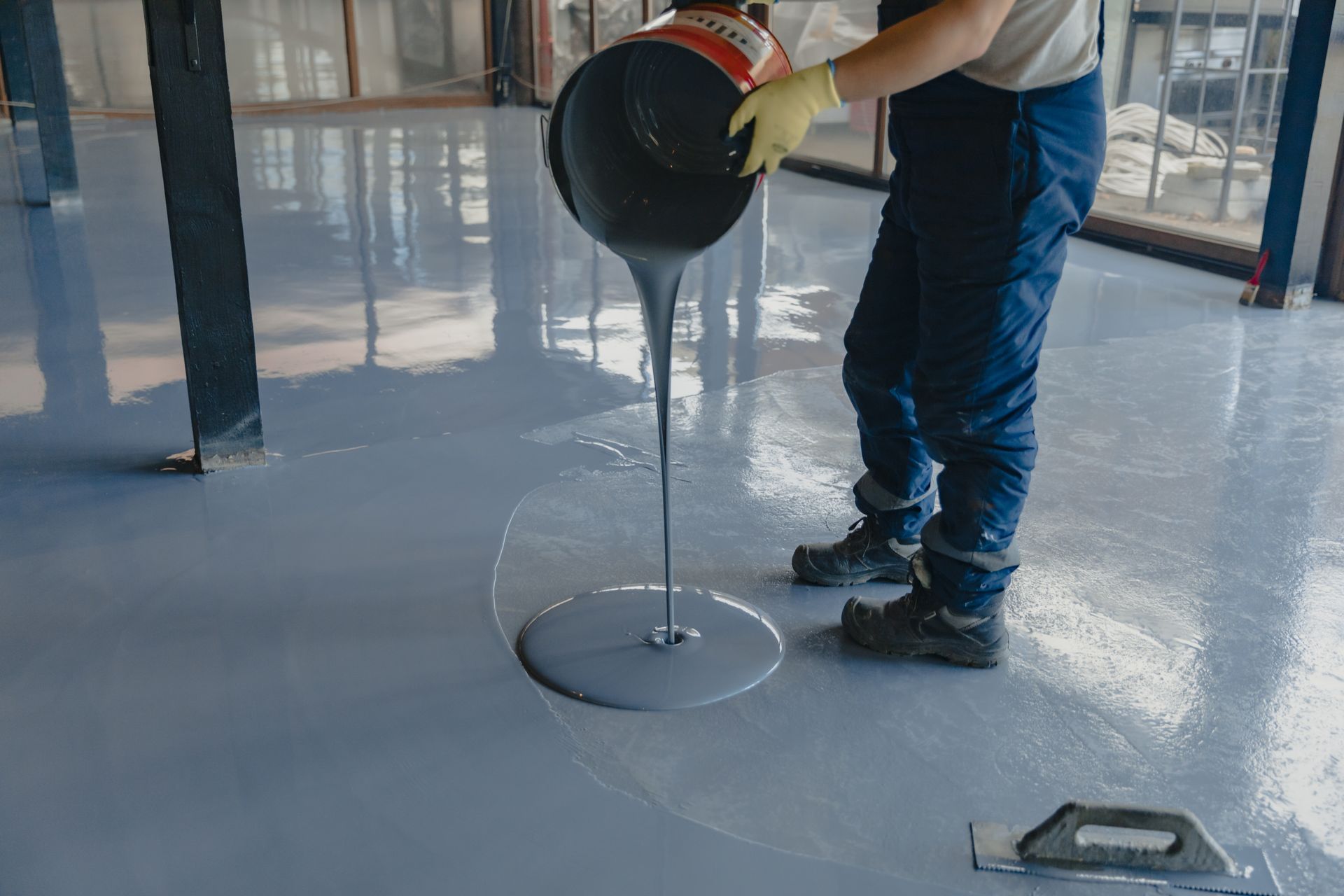 Person pouring gray epoxy coating onto a floor.