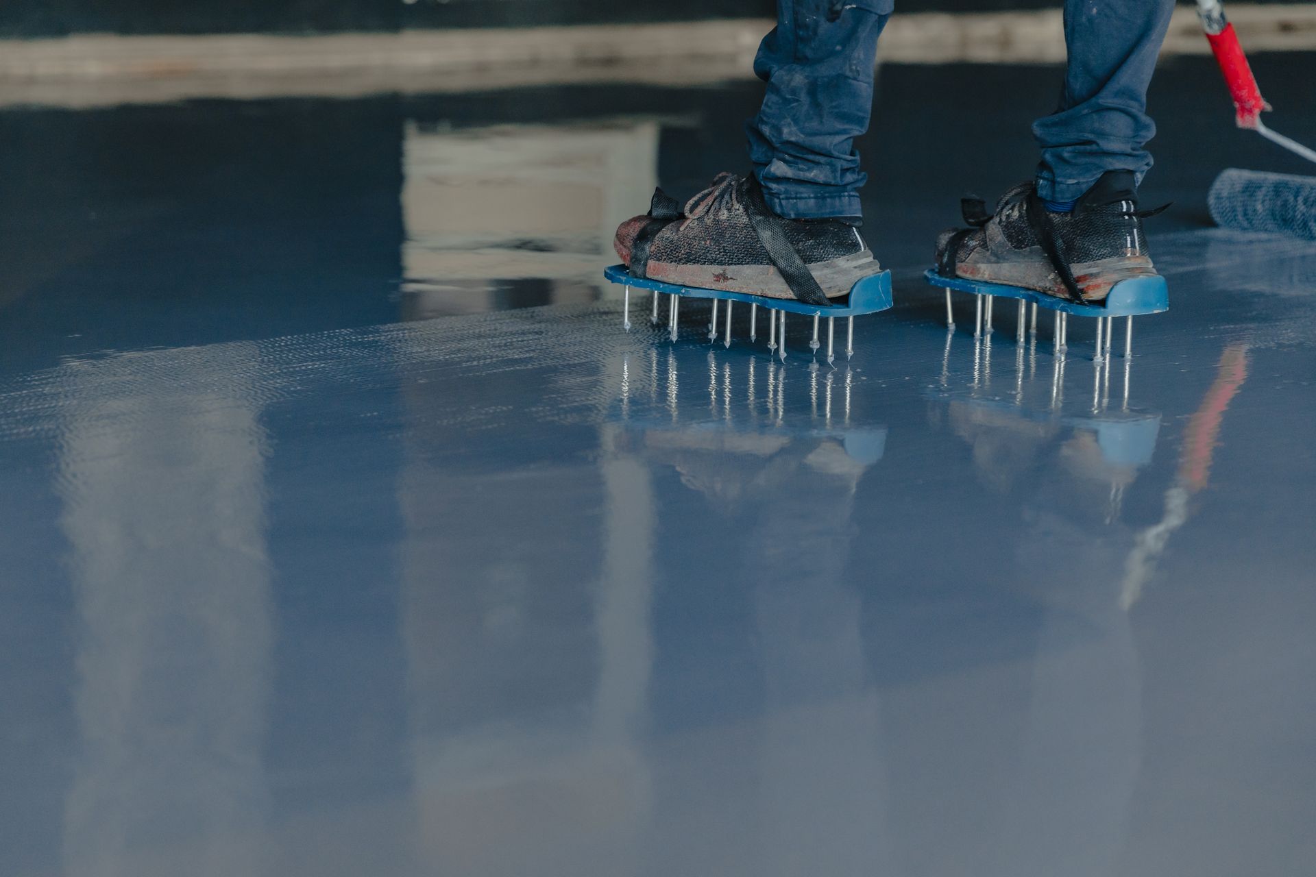 Person wearing spiked shoes on a freshly coated blue floor, likely epoxy.