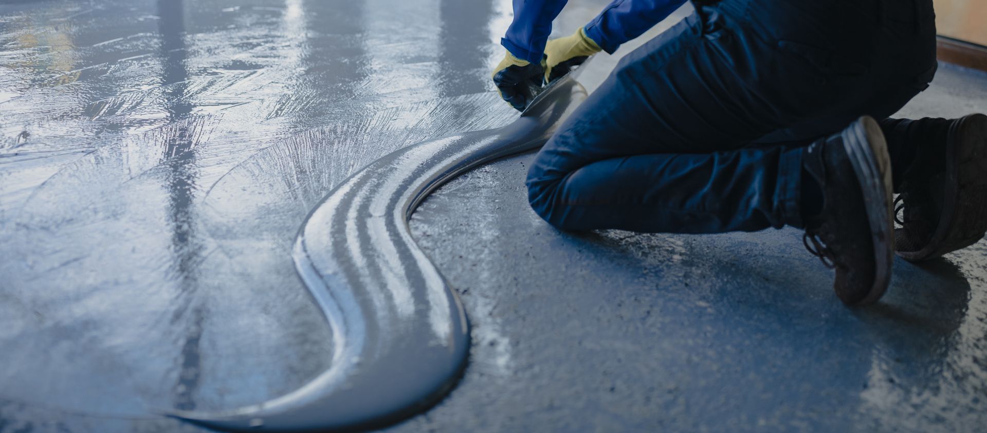 Person kneels, applying a gray sealant to a floor.