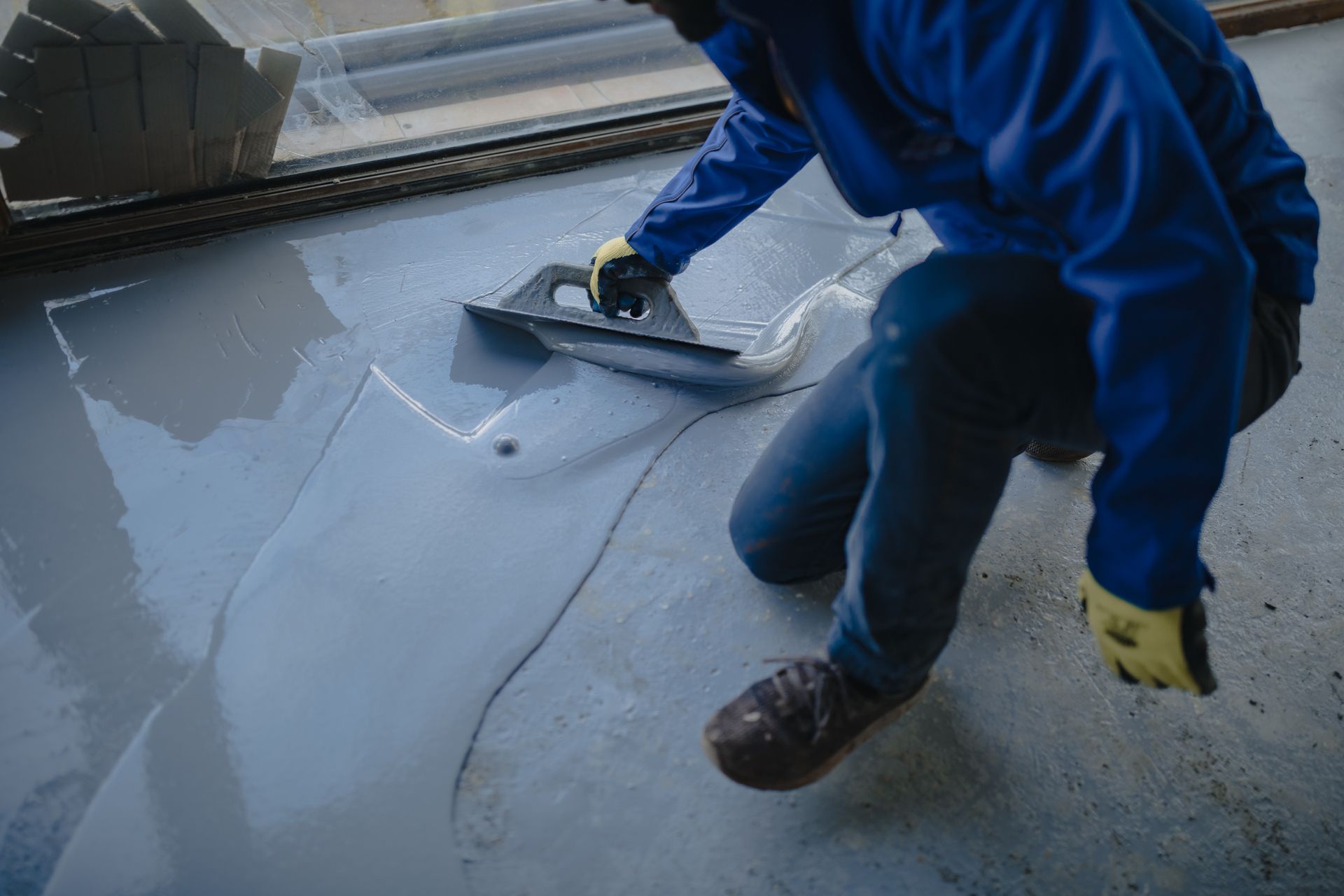 Person applying gray epoxy flooring with a trowel on a concrete floor.