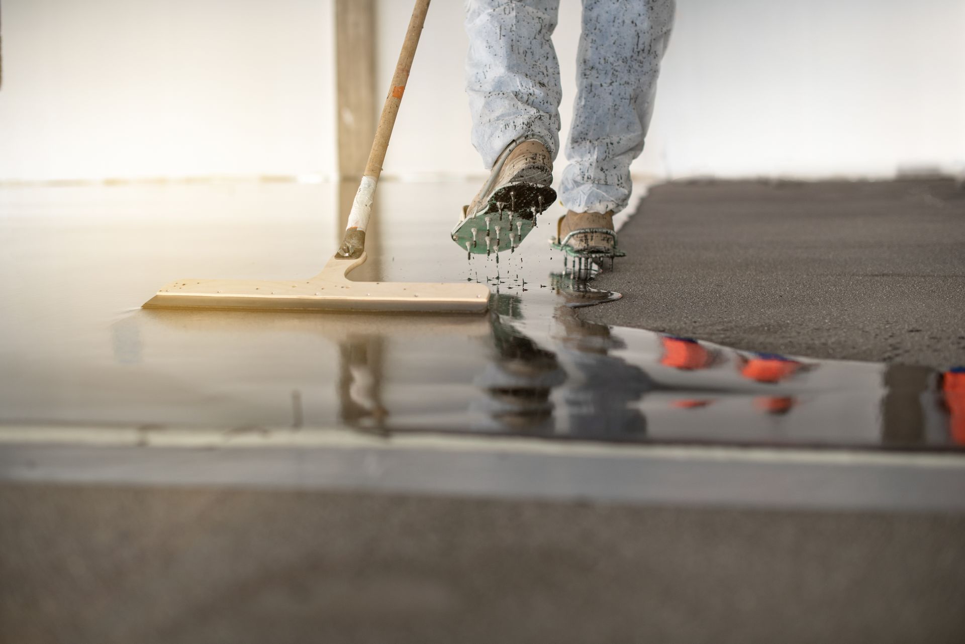 Person in paint-splattered suit smoothing epoxy on a floor with a squeegee.