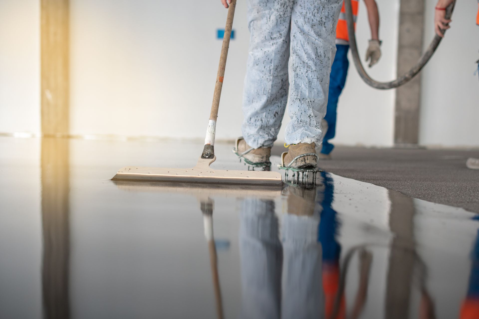Person smoothing a dark, wet coating on a floor with tools, likely for construction.