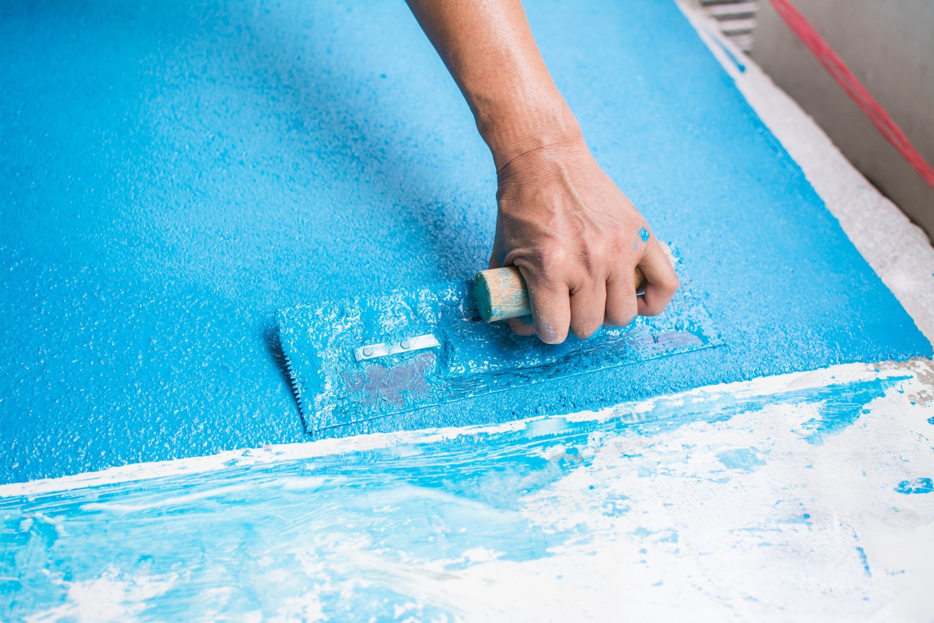 Person using a trowel to smooth blue sealant on a surface.