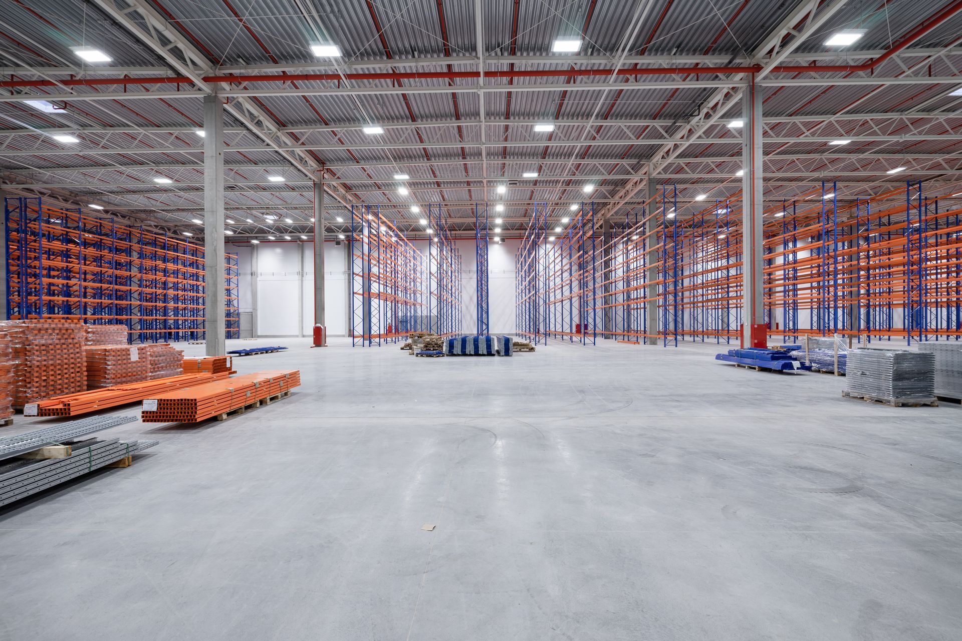 Interior of a large warehouse with shelving units, concrete floor, and overhead lights.