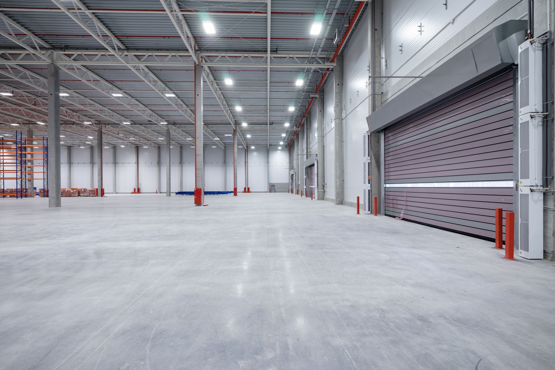 Large, empty warehouse interior with concrete floor, metal beams, and roll-up door.
