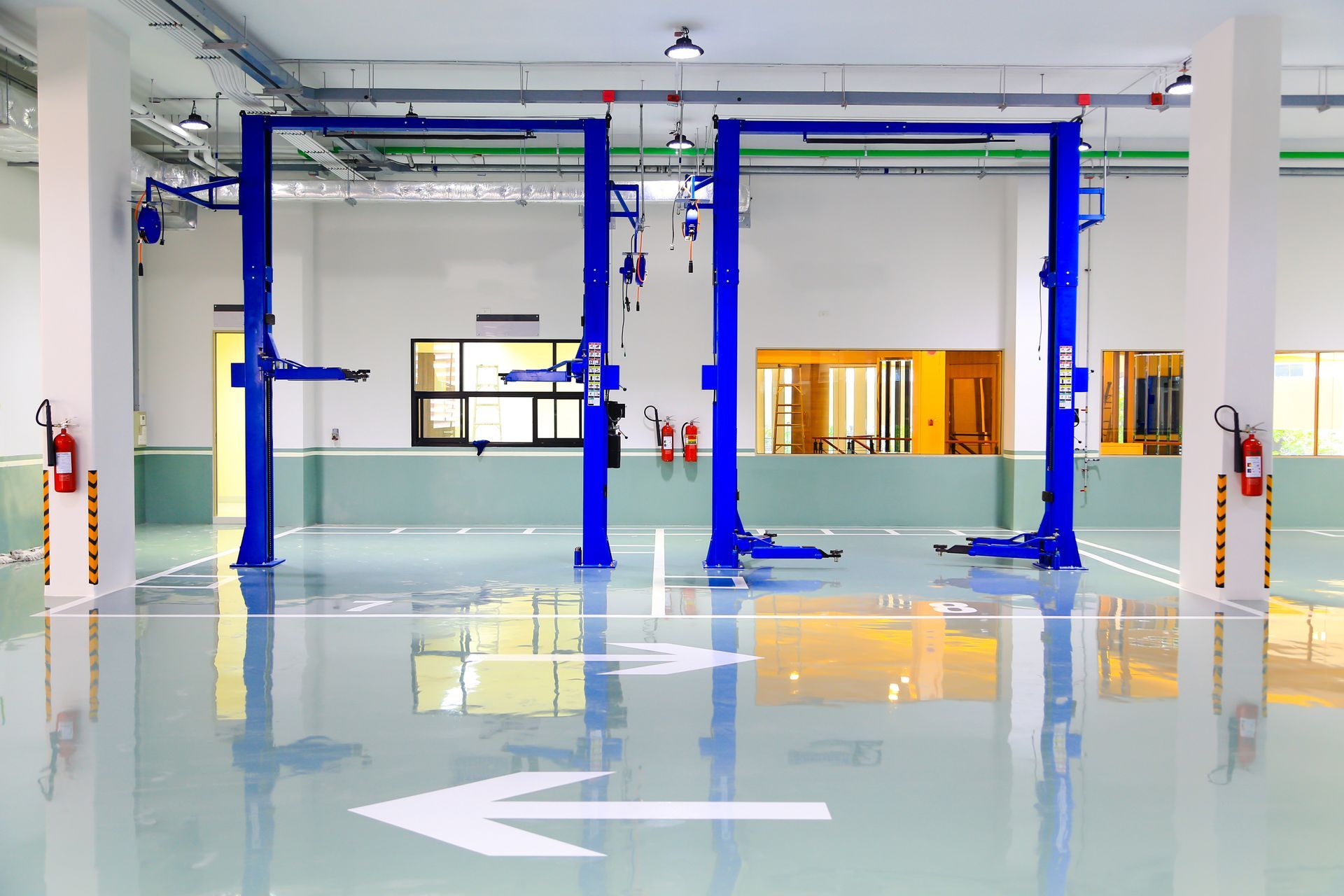 Blue car lifts in a bright, modern auto repair shop with white walls and a reflective floor.