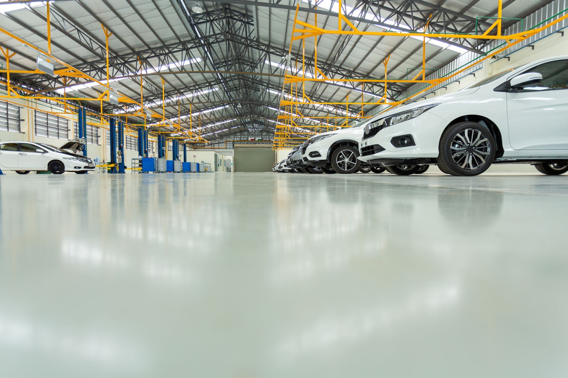 A light-colored, spacious auto repair shop with white cars parked on a shiny gray floor.