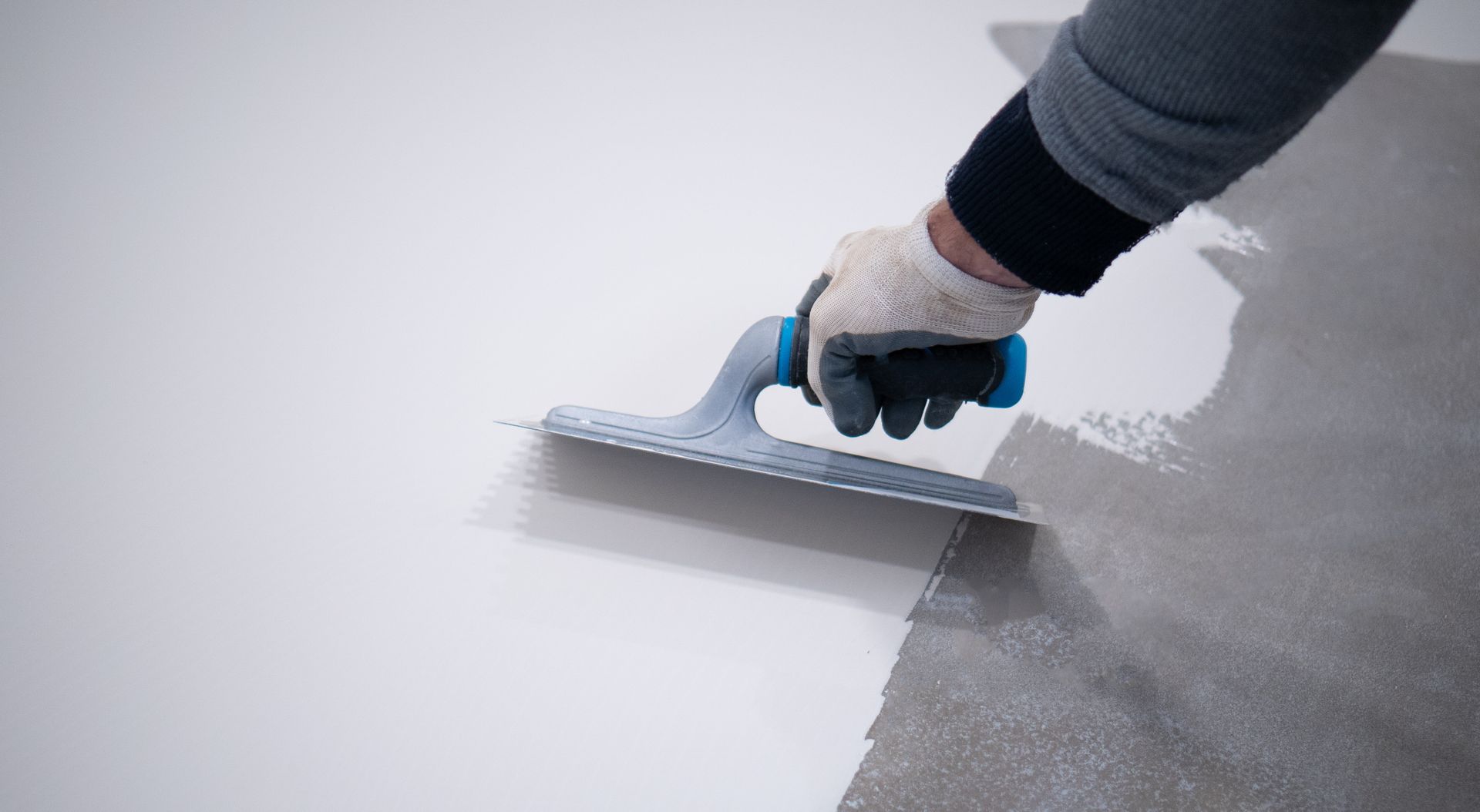 Person using a trowel to apply a gray substance to a white surface.