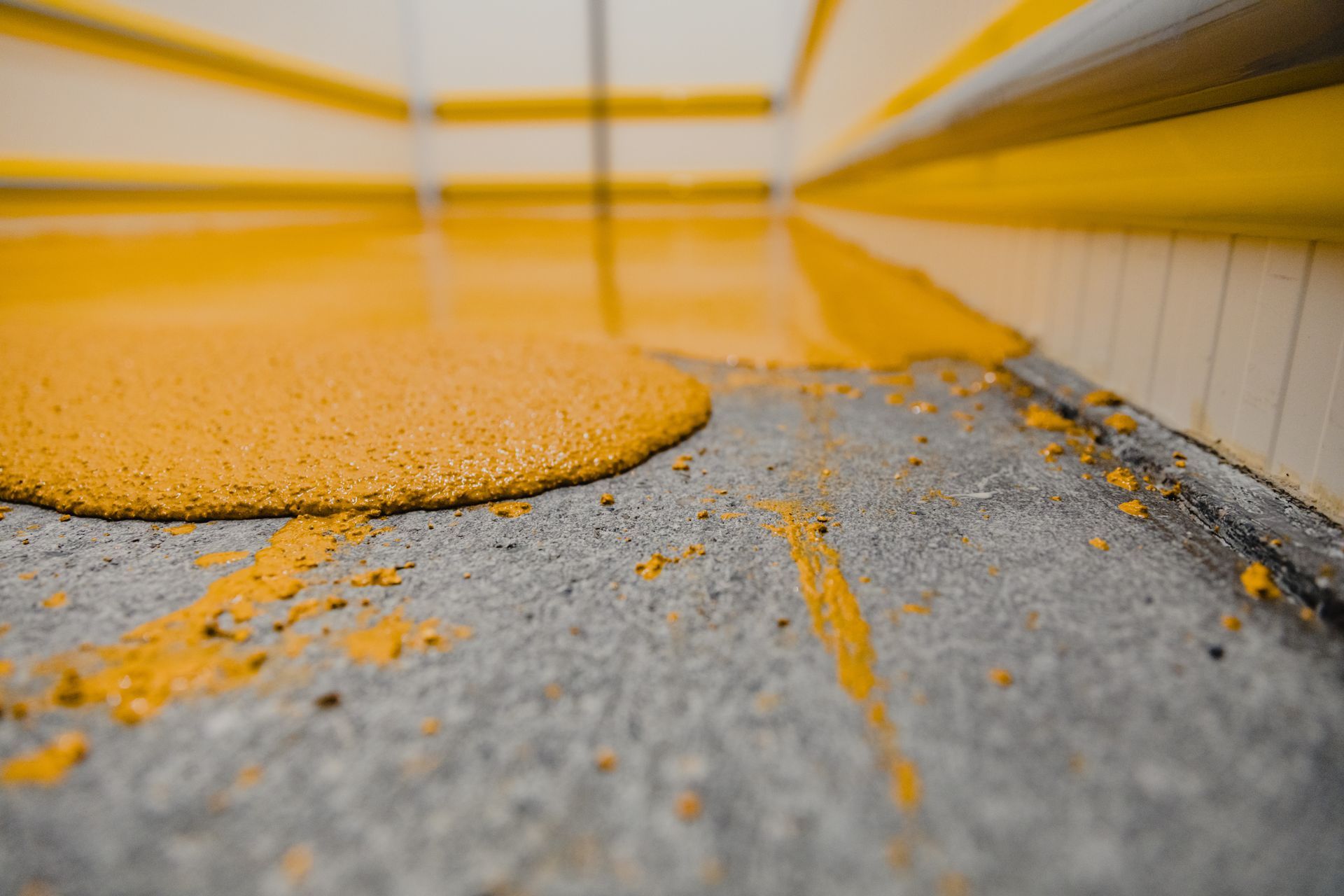 Yellow epoxy coating spilling onto a gray concrete floor in a room with yellow and white walls.